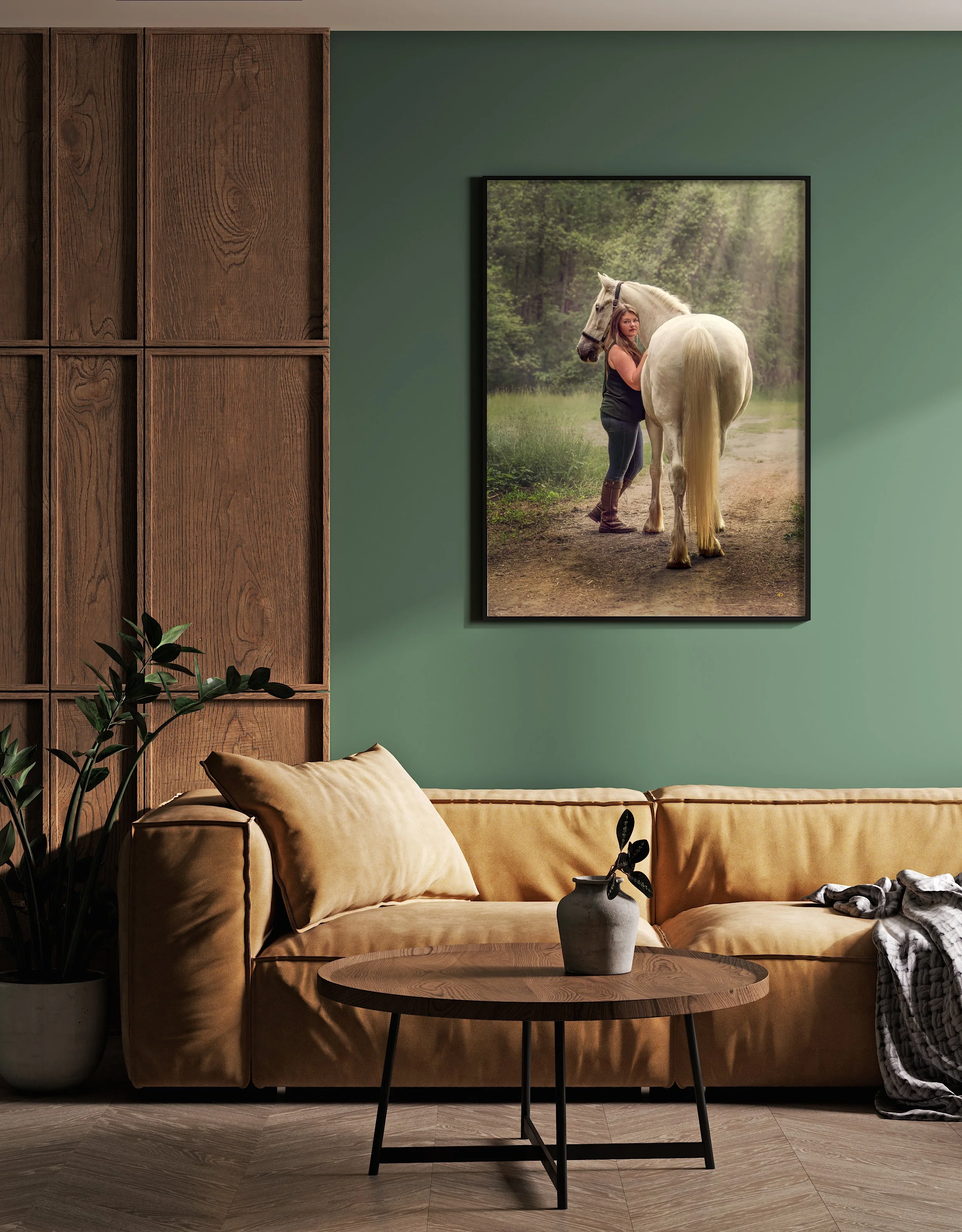Living room with beige sofa, wooden coffee table with a vase, a plant, and a framed photo of a woman with a horse on a green forest background hanging on the wall.