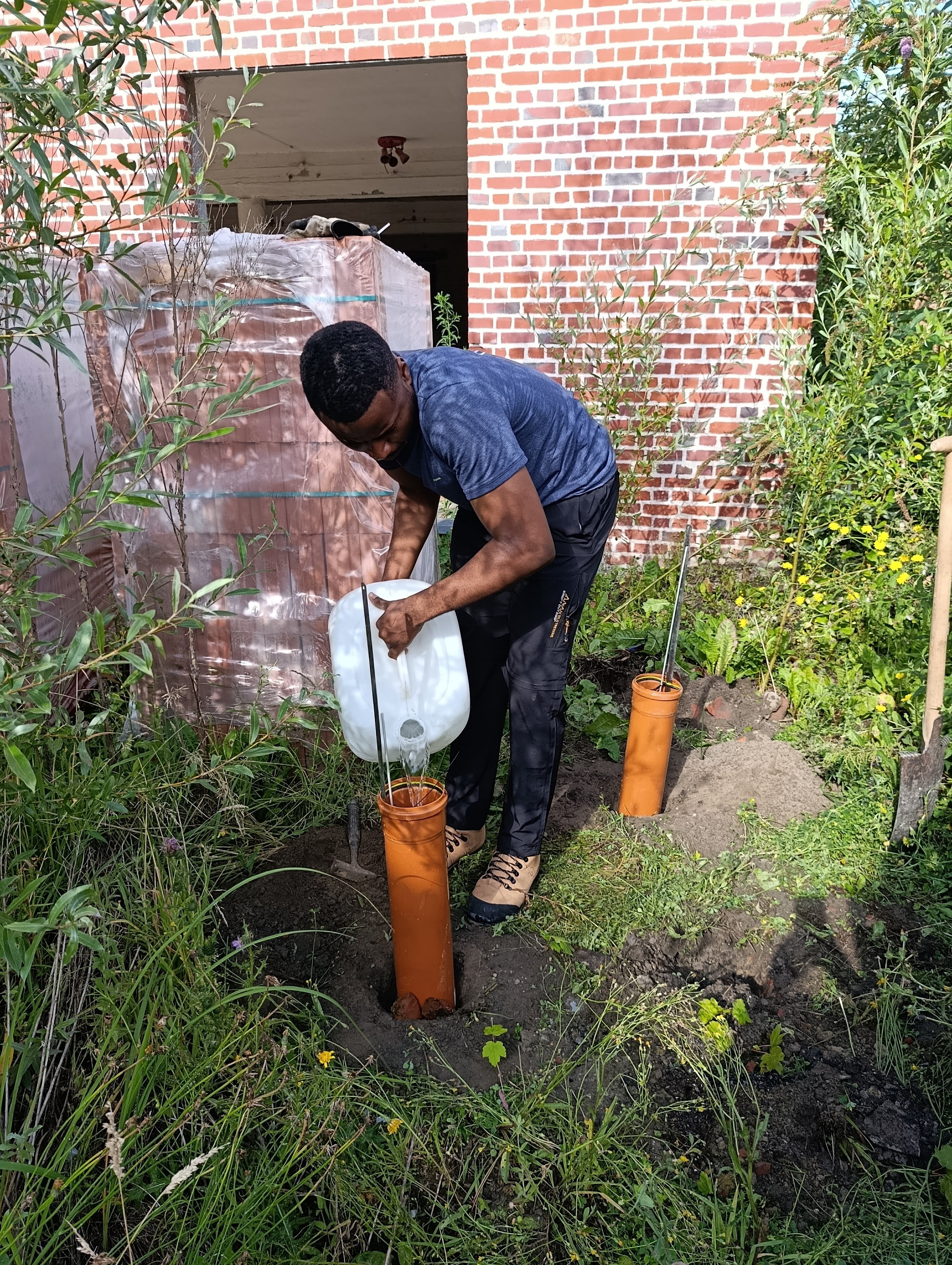 Photographie de Maurel injectant de l'eau dans un tube d'infiltration en plastique afin de tester la perméabilité du sol.