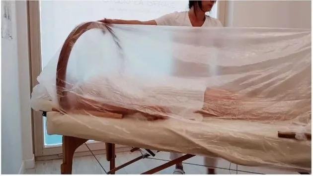 Persona stesa su un lettino da massaggio, coperta da un telo trasparente in un ambiente luminoso.