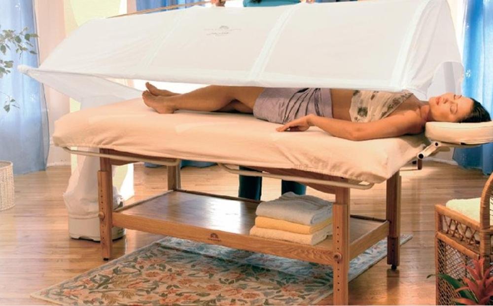 Donna su un lettino da massaggio con telo per sauna, in un ambiente rilassante.