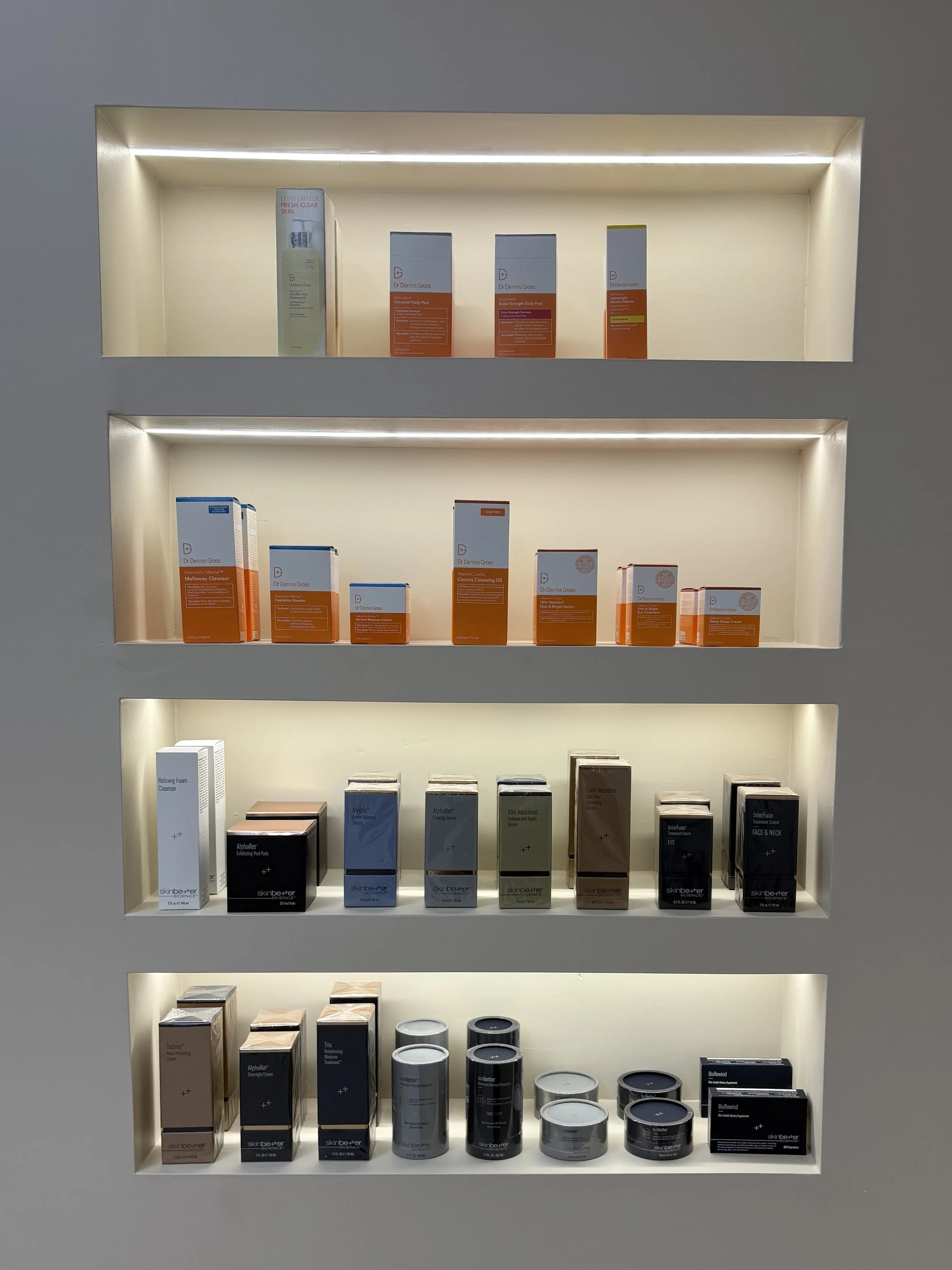 Display of skincare products on illuminated shelves, including cleansers, oils, and creams in various packaging.