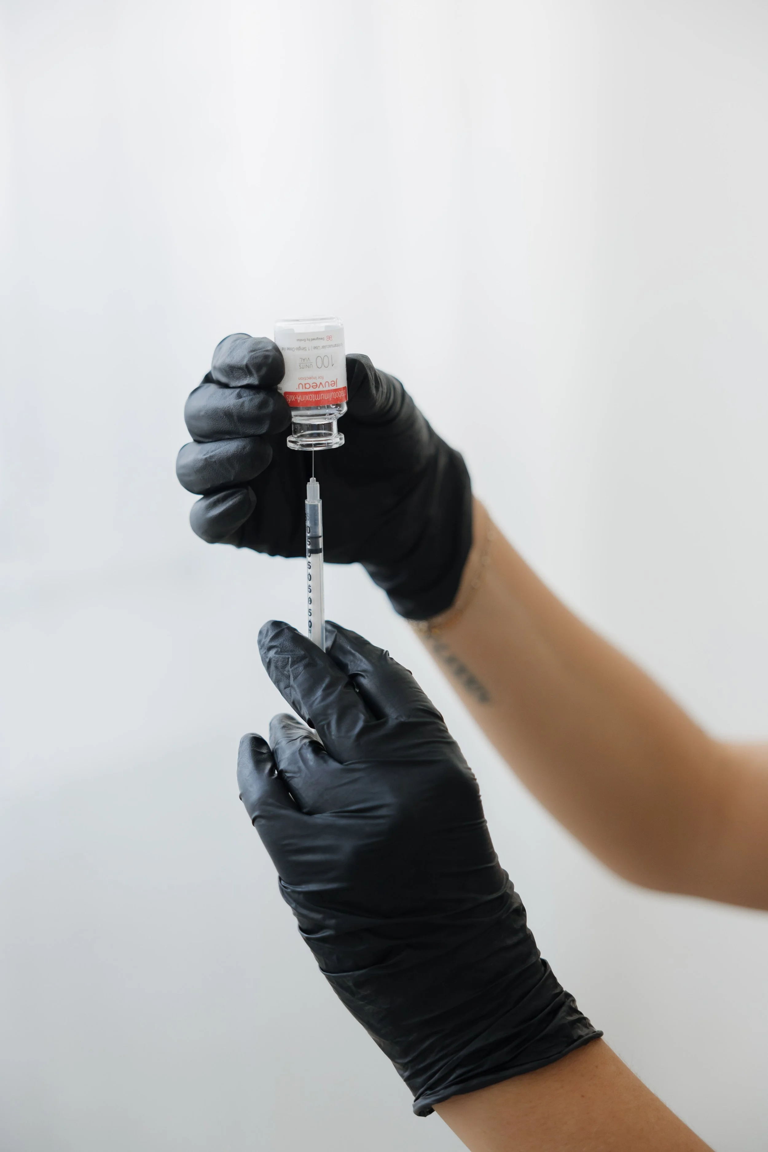 A person wearing black gloves drawing a vaccine from a vial into a syringe.