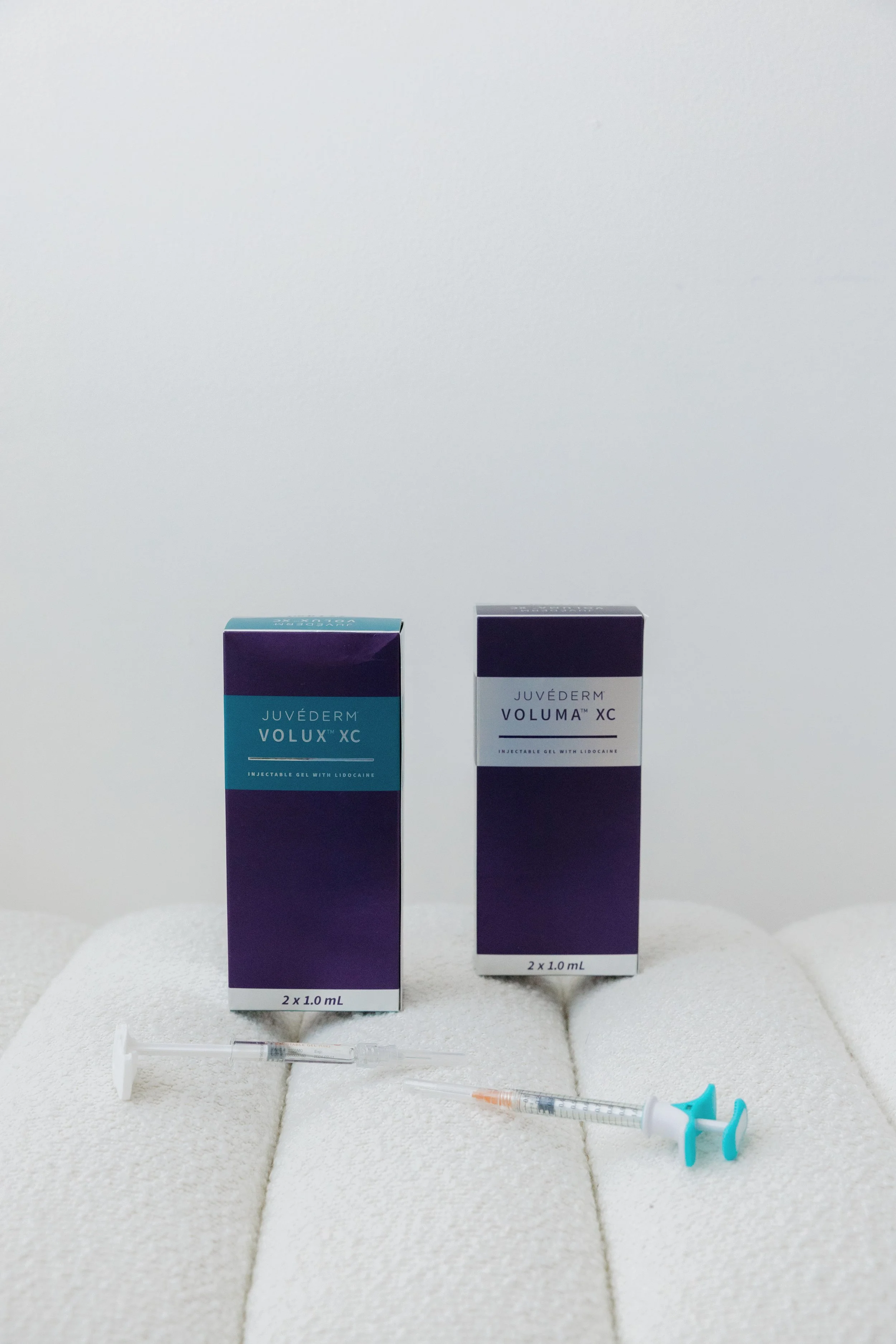 Two boxes of Juvederm Volux XC dermal filler, with one syringe placed on a white cushioned surface in front of each box.