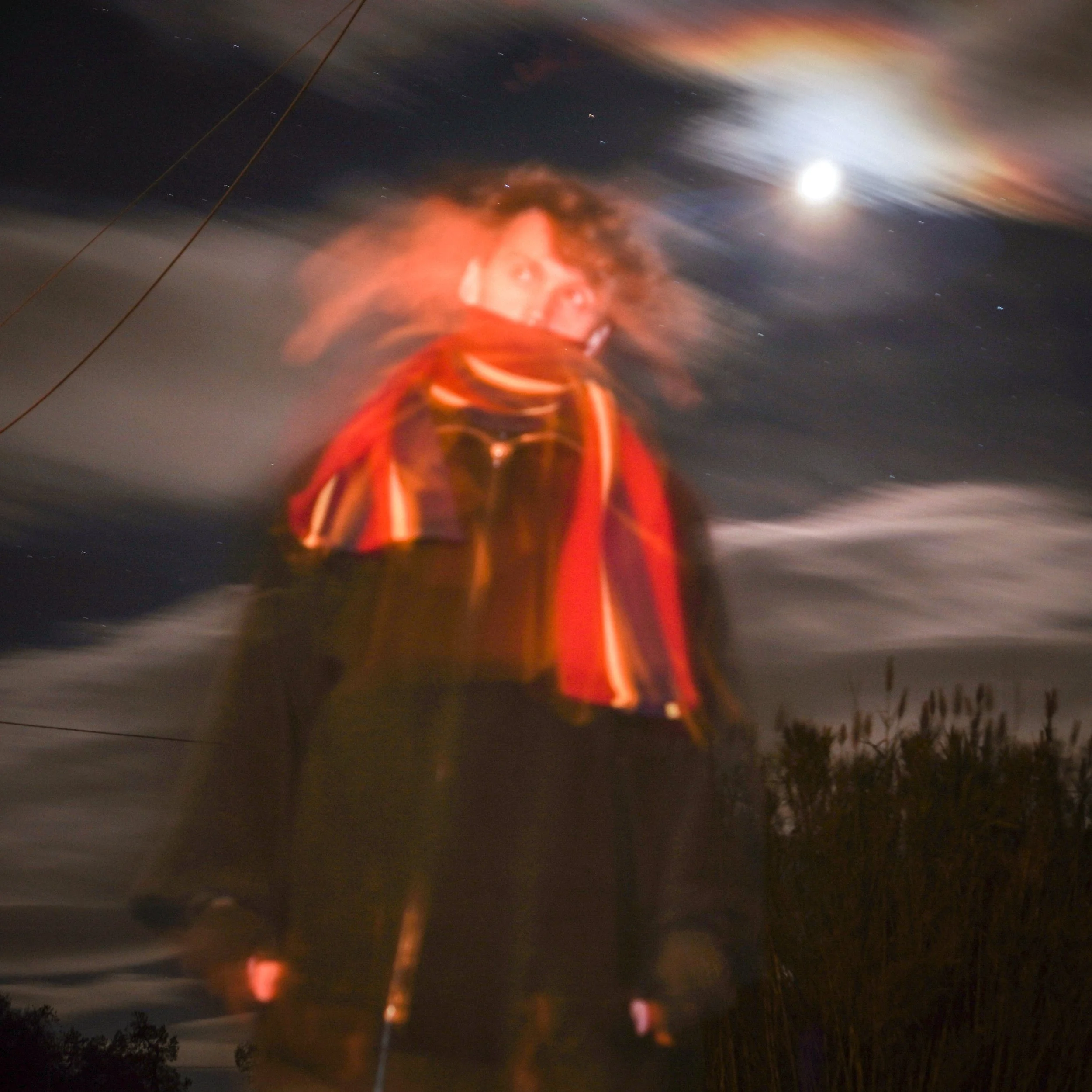 Storm Elfrink - Photography - Blurred night sky with a full moon, some clouds, and distant stars, viewed from ground level with trees and power lines in the foreground.