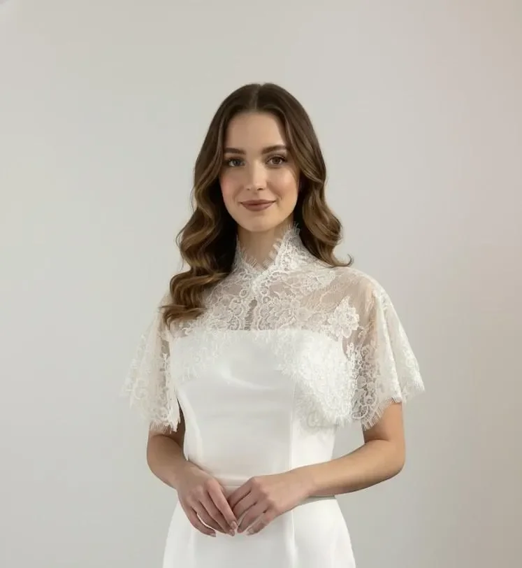 A young woman in a white lace dress standing against a plain gray background, smiling at the camera.