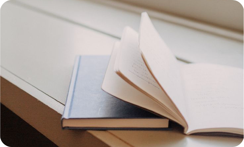 Un libro abierto sobre otro libro en una mesa junto a una ventana