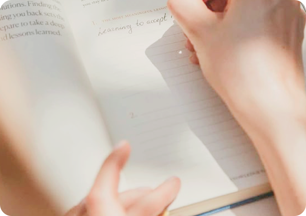 Una mano escribe en una libreta o cuaderno con líneas. La otra mano sostiene la página para mantenerla abierta.