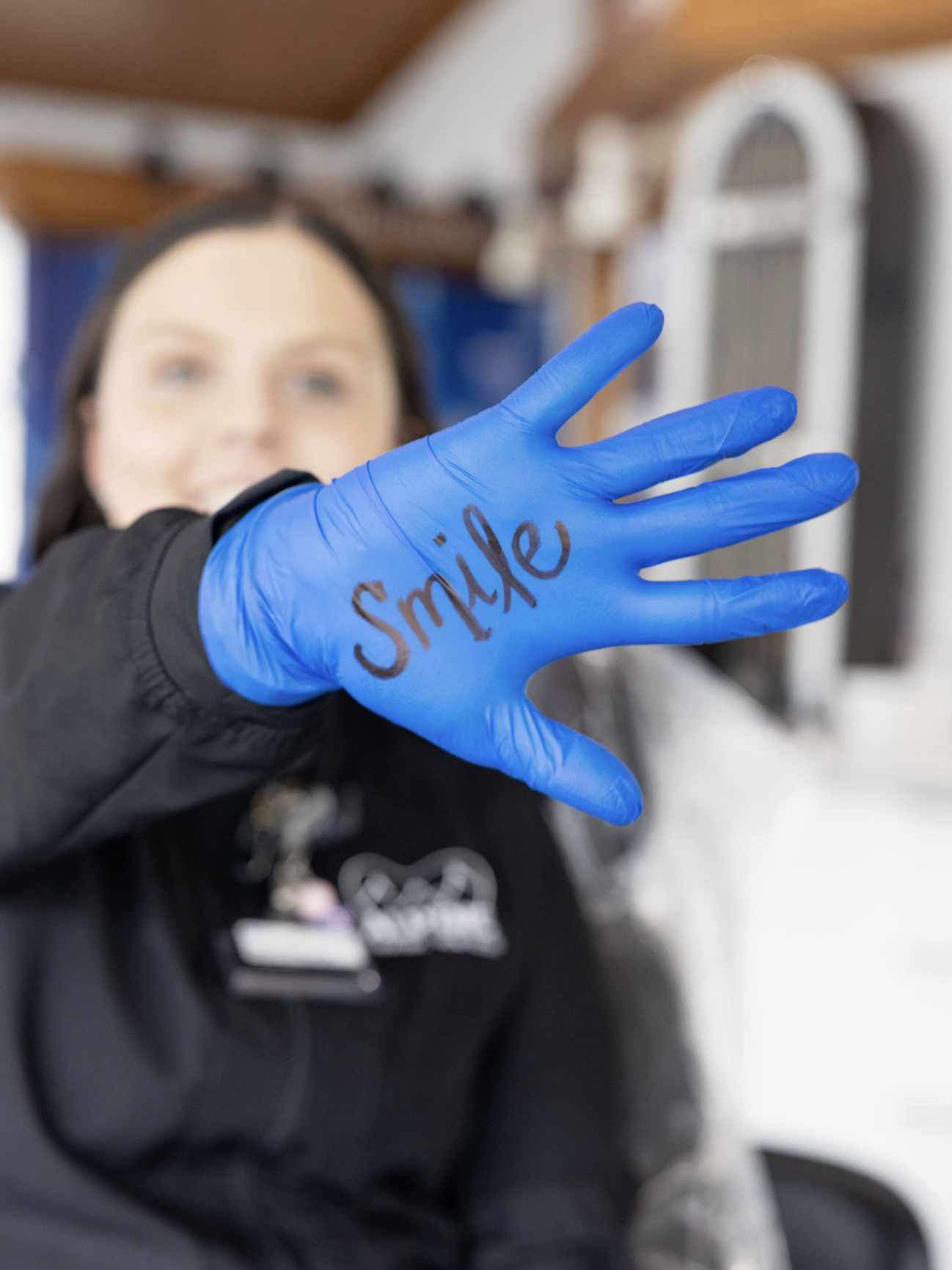 Dental Assistant is holding up a glove that says "Smile"