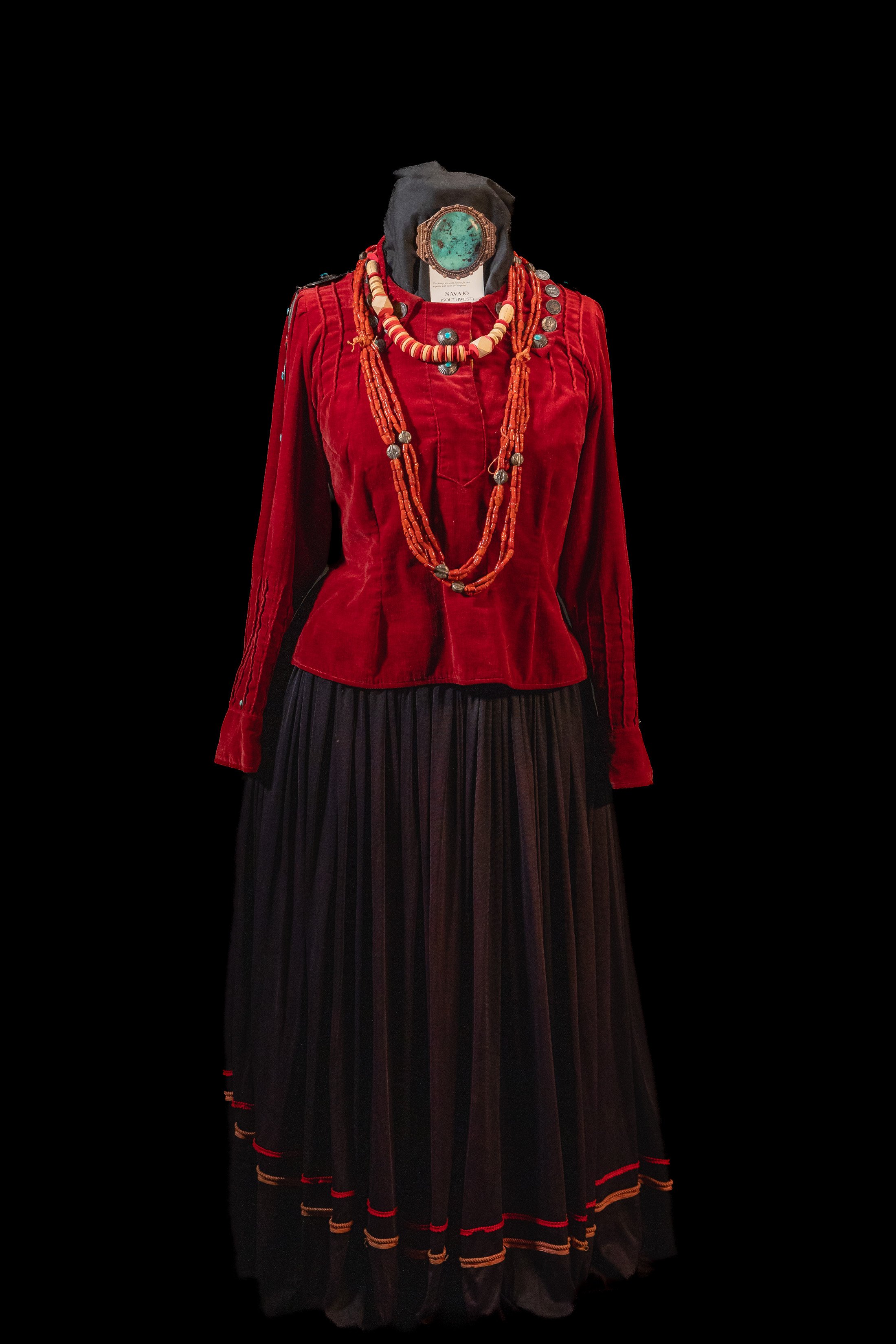Traditional ethnic clothing with a red velvet top and long black skirt adorned with necklaces.