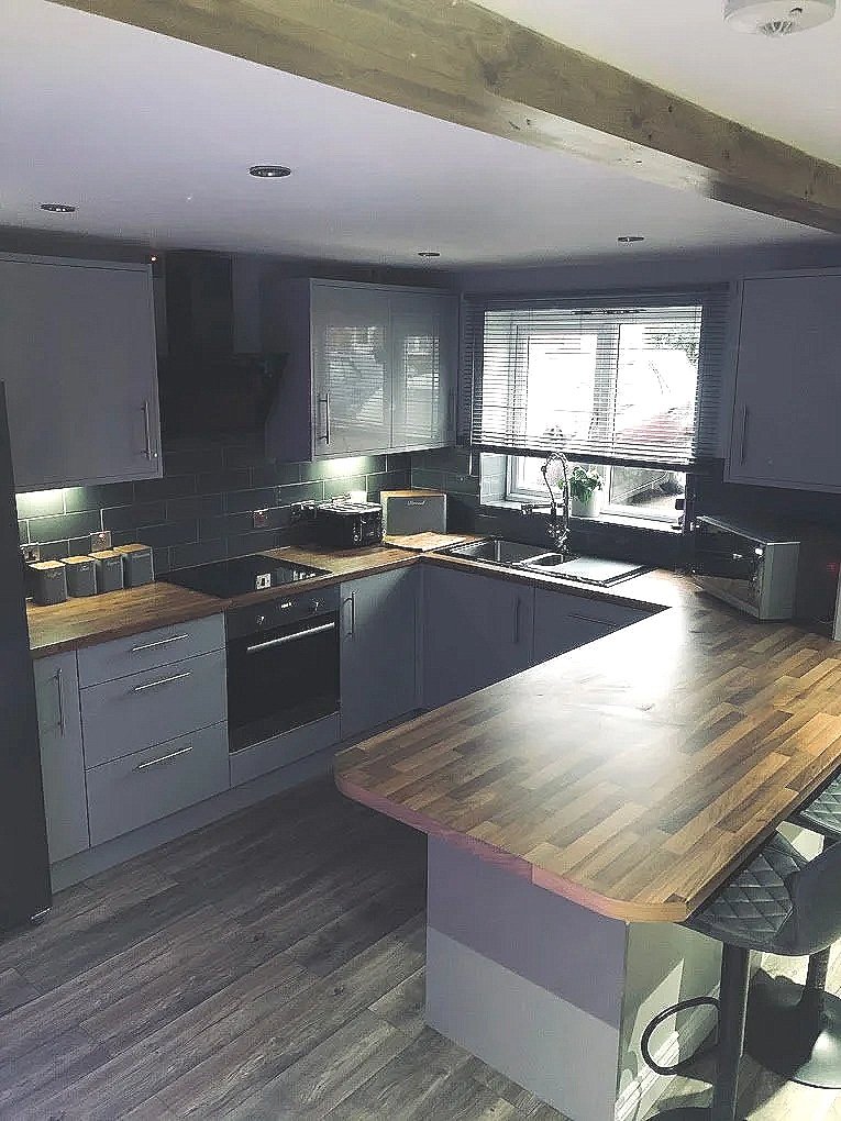 Modern kitchen with gray cabinets, wooden countertops, a window with blinds, and a kitchen island with a wooden surface.