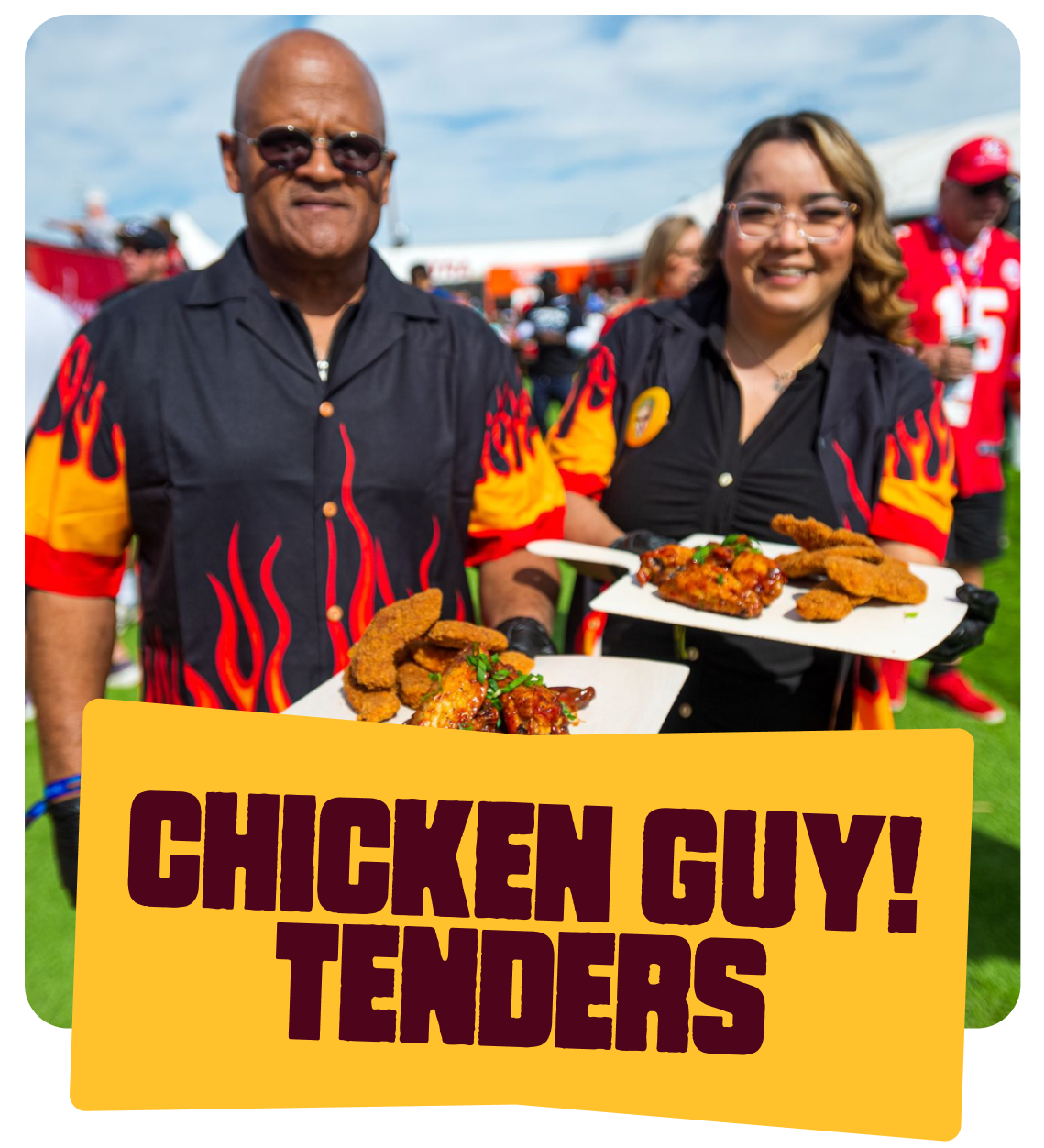 Two smiling people in flame-themed shirts holding trays of fried chicken and tenders at an outdoor event with a crowd and a football field in the background. A sign in front reads 'Chicken Guy! Tenders'.