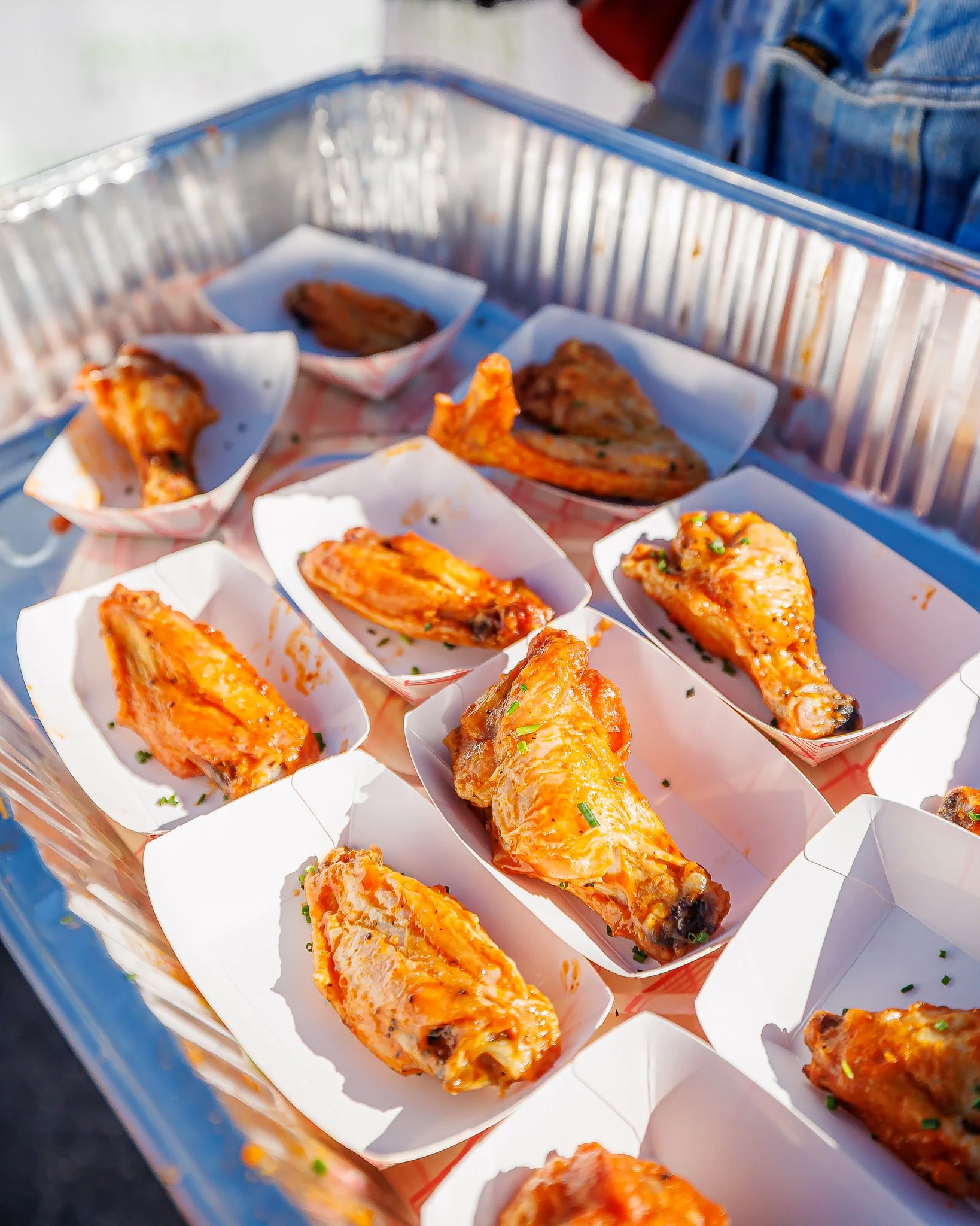 Tray of baked spicy chicken wings on paper trays at an outdoor event.