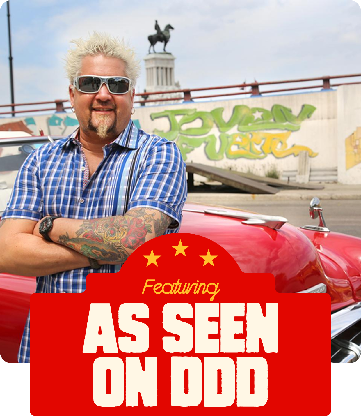 A man with spiky blond hair, sunglasses, and tattoos on his arms, standing with arms crossed in front of a red vintage car, with a mural and the Washington Monument in the background. The image features a red banner with yellow stars and the text 'Featuring As Seen on DDD'.