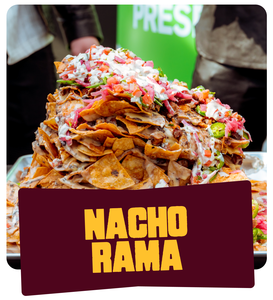 A large display of nachos topped with cheese, sour cream, chopped vegetables, and other toppings at a food event.