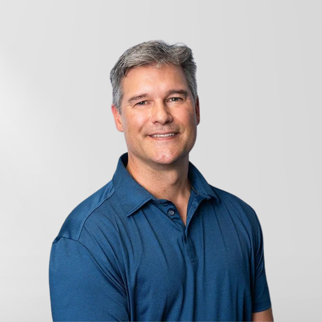 Man in a blue polo shirt smiling against a light background.
