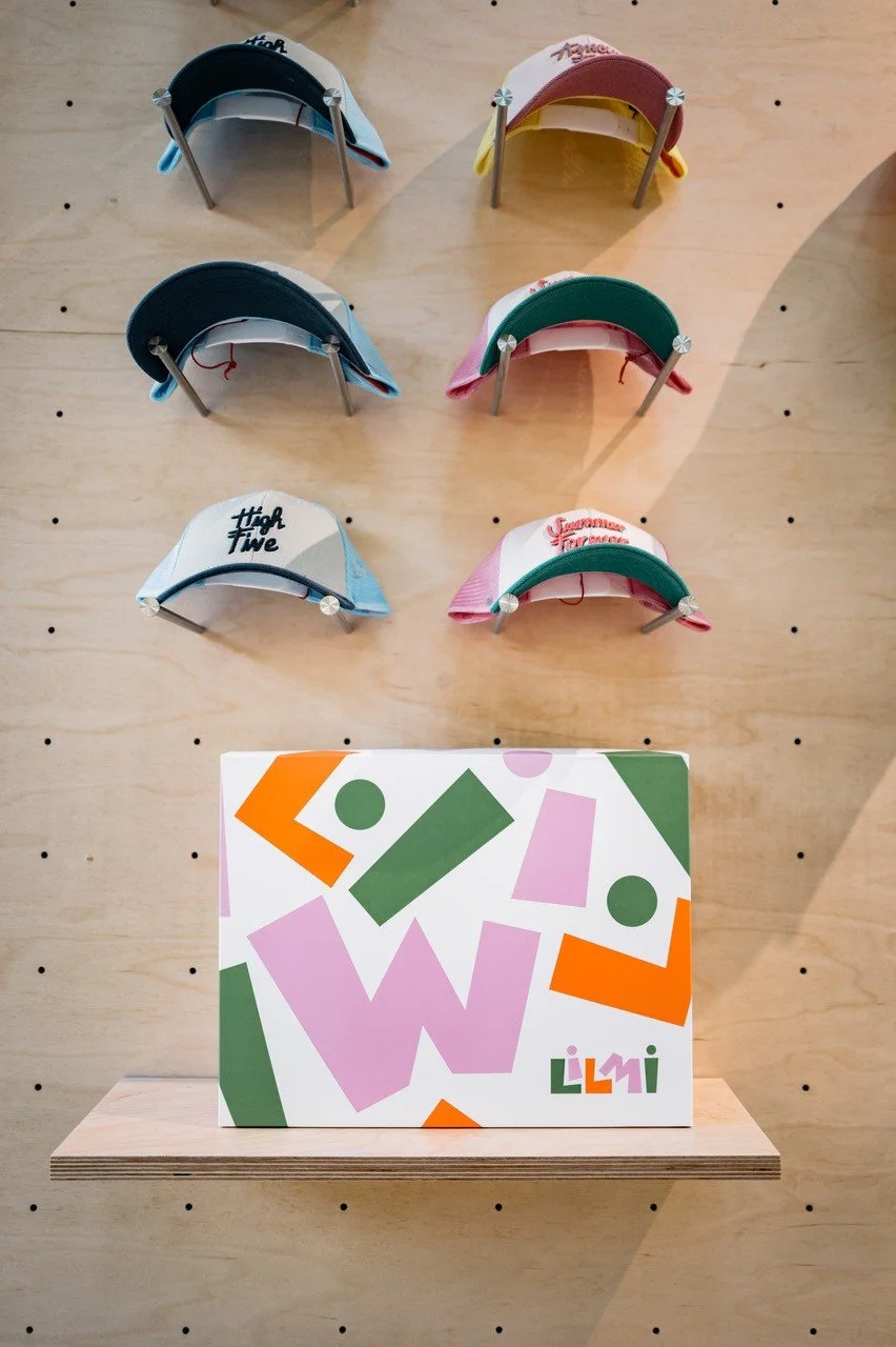 Display of six colorful caps arranged on a wooden wall with a shelf holding a Lilly pulitzer box at the bottom.