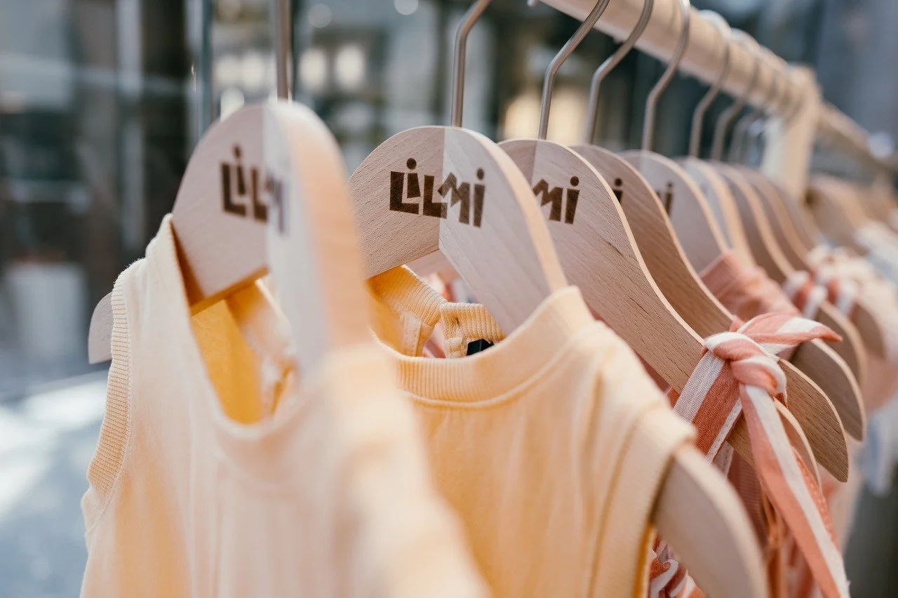 Several wooden hangers on a clothing rack, each holding a pastel-colored children's shirt, in a retail store.