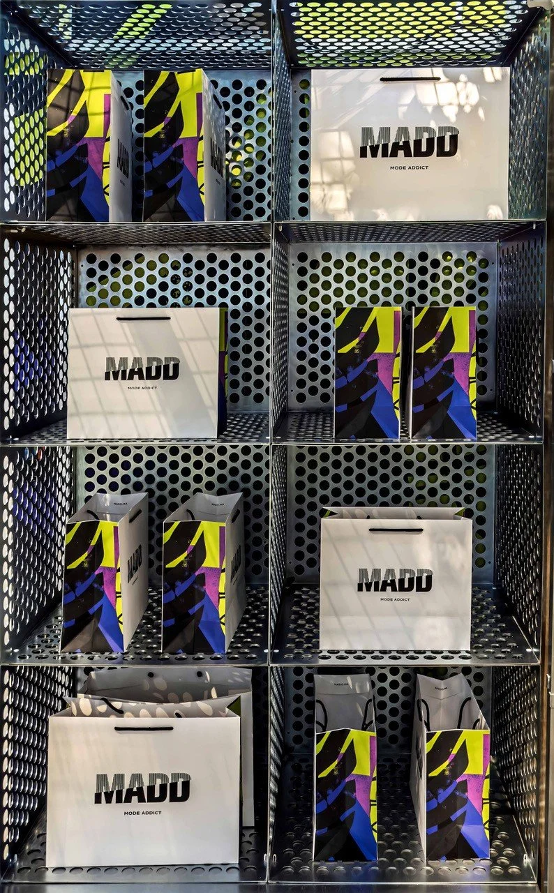 Retail display with black metal shelves containing MADD boxes and shopping bags with a black, white, yellow, purple, and blue design.