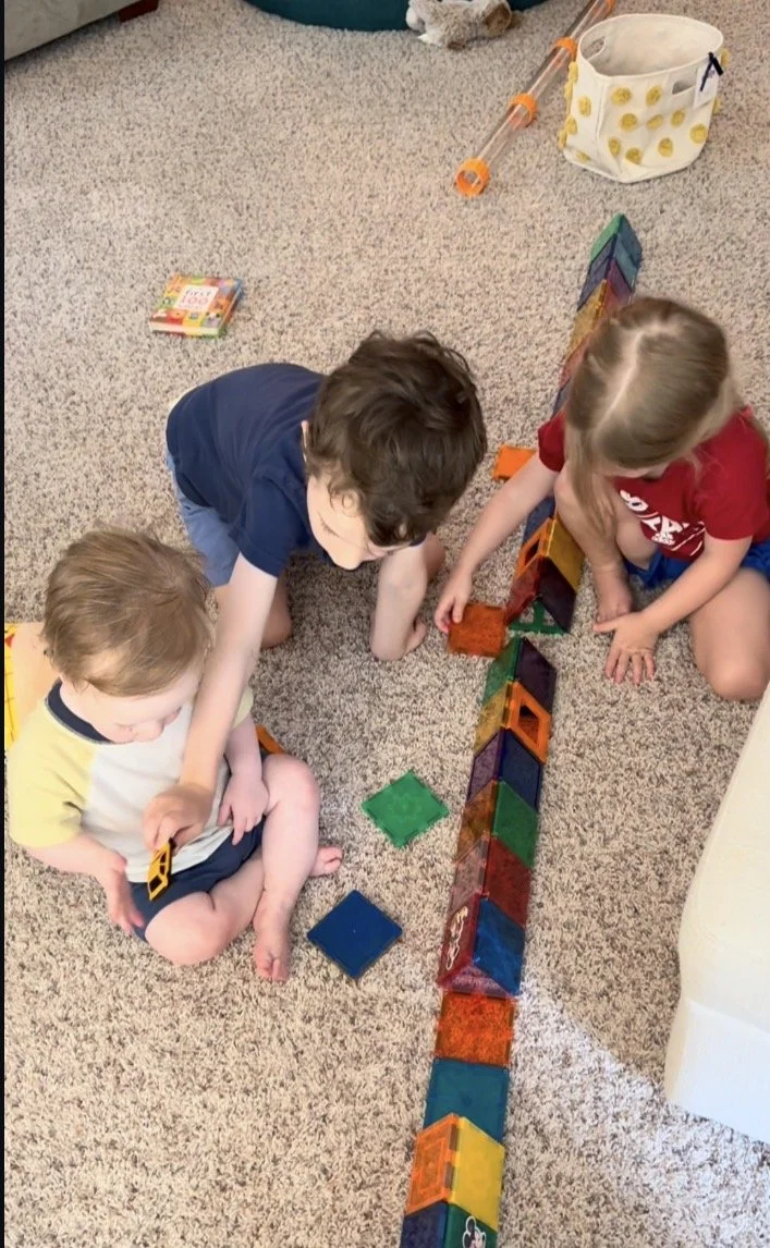 three kids building with rainbow magnet tiles on the living room floor