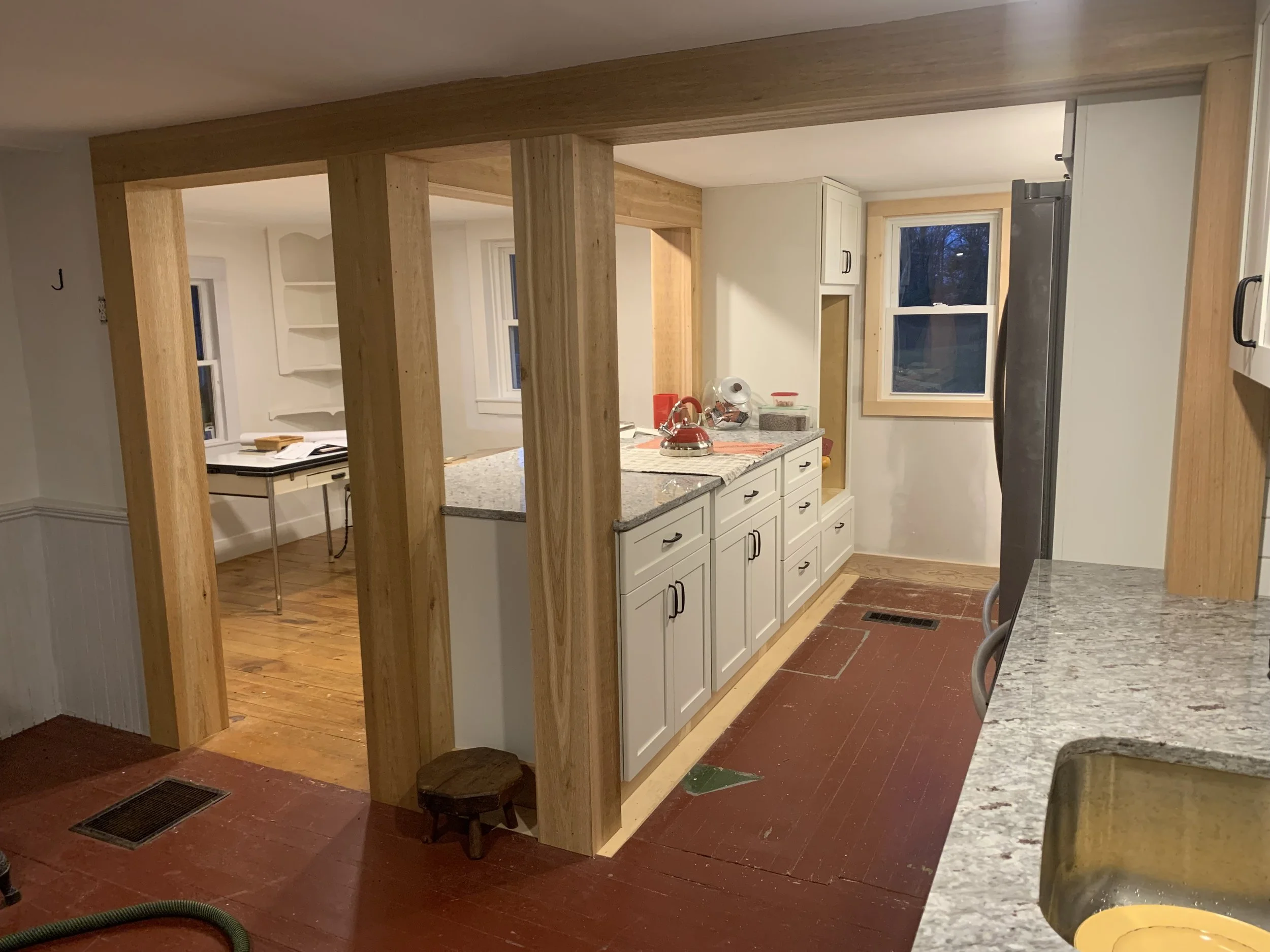 Kitchen with white cabinets, a granite countertop, wooden framing, a window, and a stainless steel refrigerator