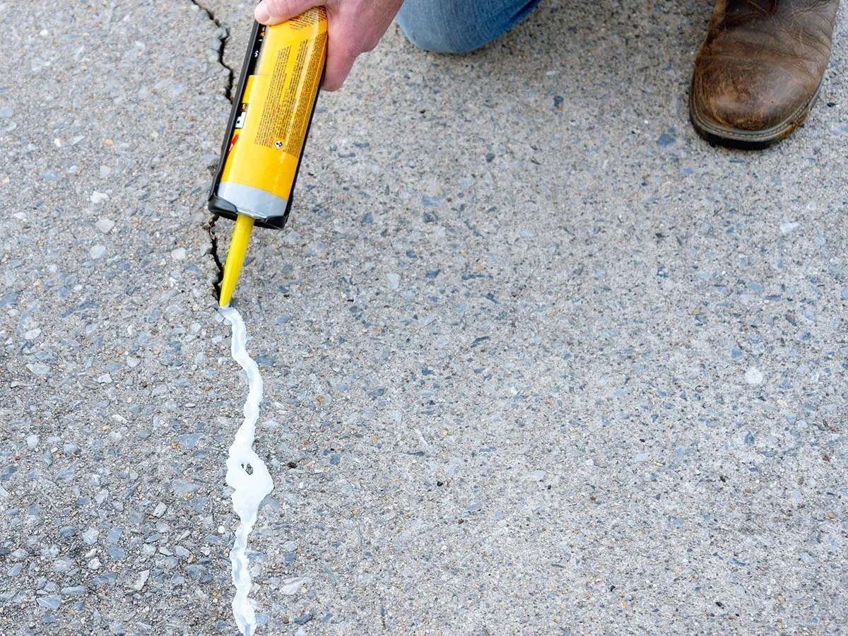 Person applying crack filler to a crack in a concrete sidewalk with a caulking gun.