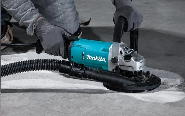 Person using a blue Makita electric planer on a concrete surface.