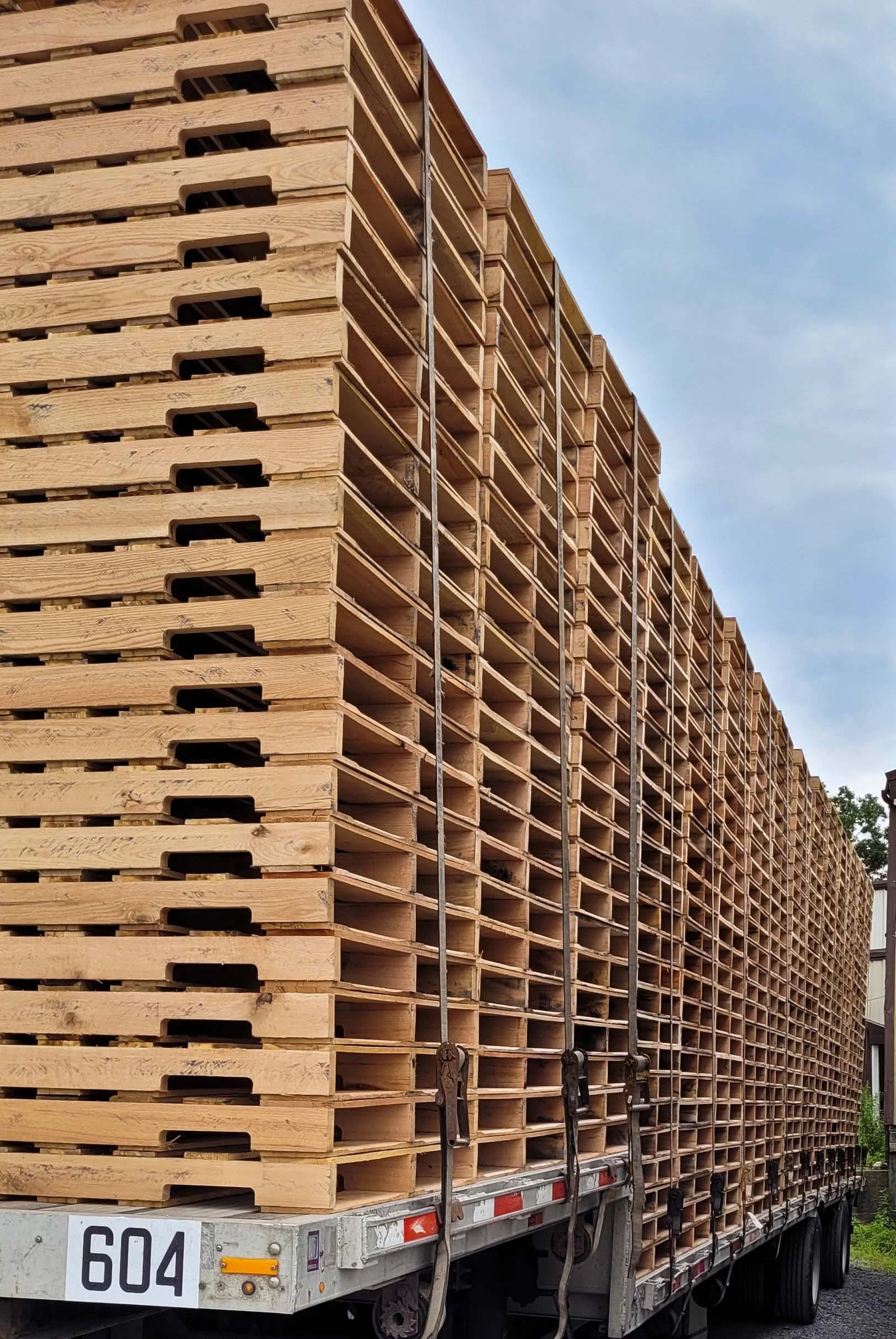 stacks of pallets tied down with ratchet straps on a step-deck trailer