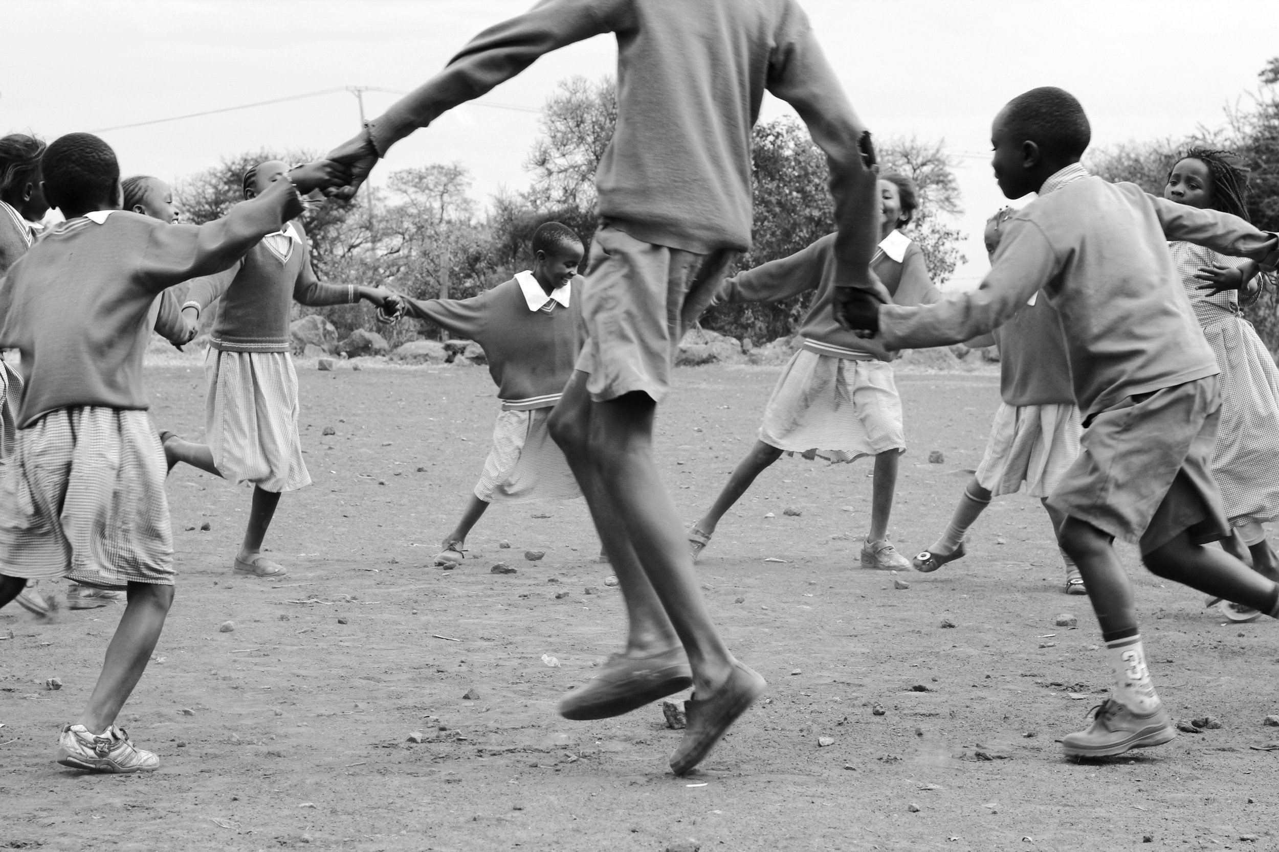 Children in school uniforms playing a game in an outdoor field, holding hands and forming a circle.