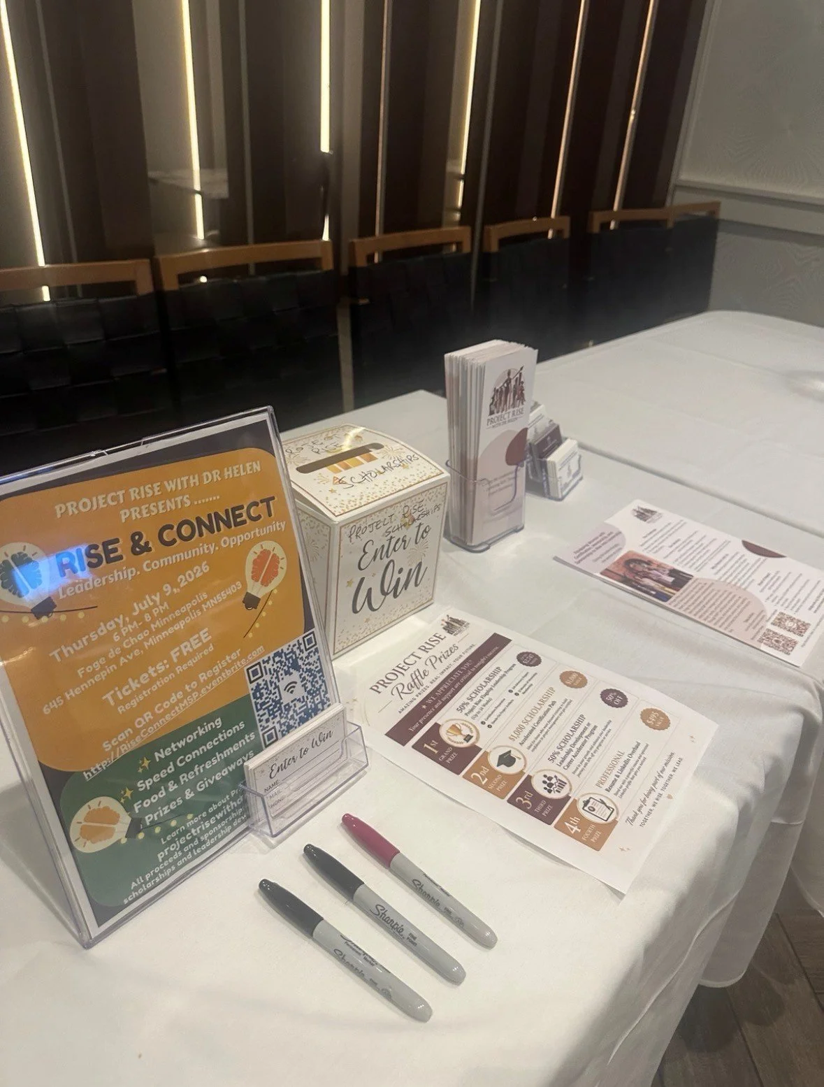Registration table for the event 'Rise & Connect' with flyers, sign-up sheets, and raffle entry boxes at the project rise event.