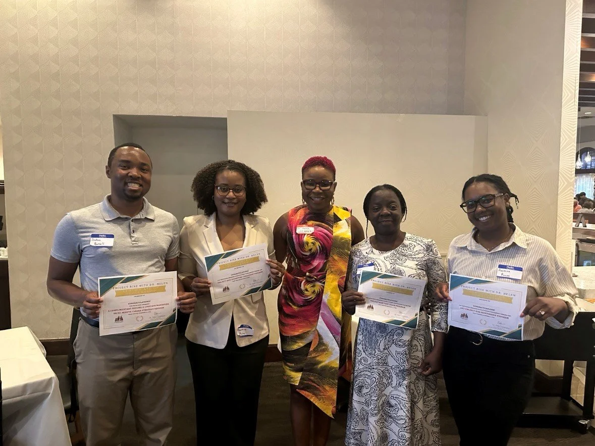Five people standing indoors, holding certificates and smiling, at an award or certificate presentation event.
