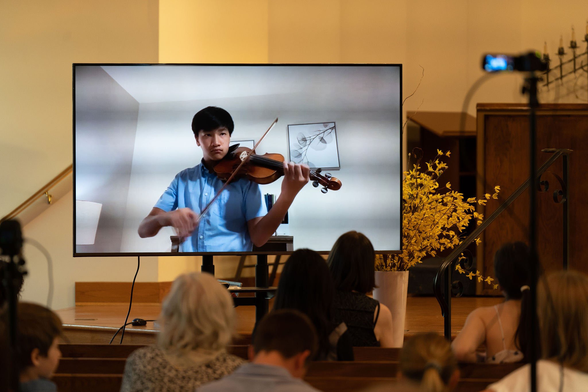 A teenage boy plays violin in a video at a recital performance