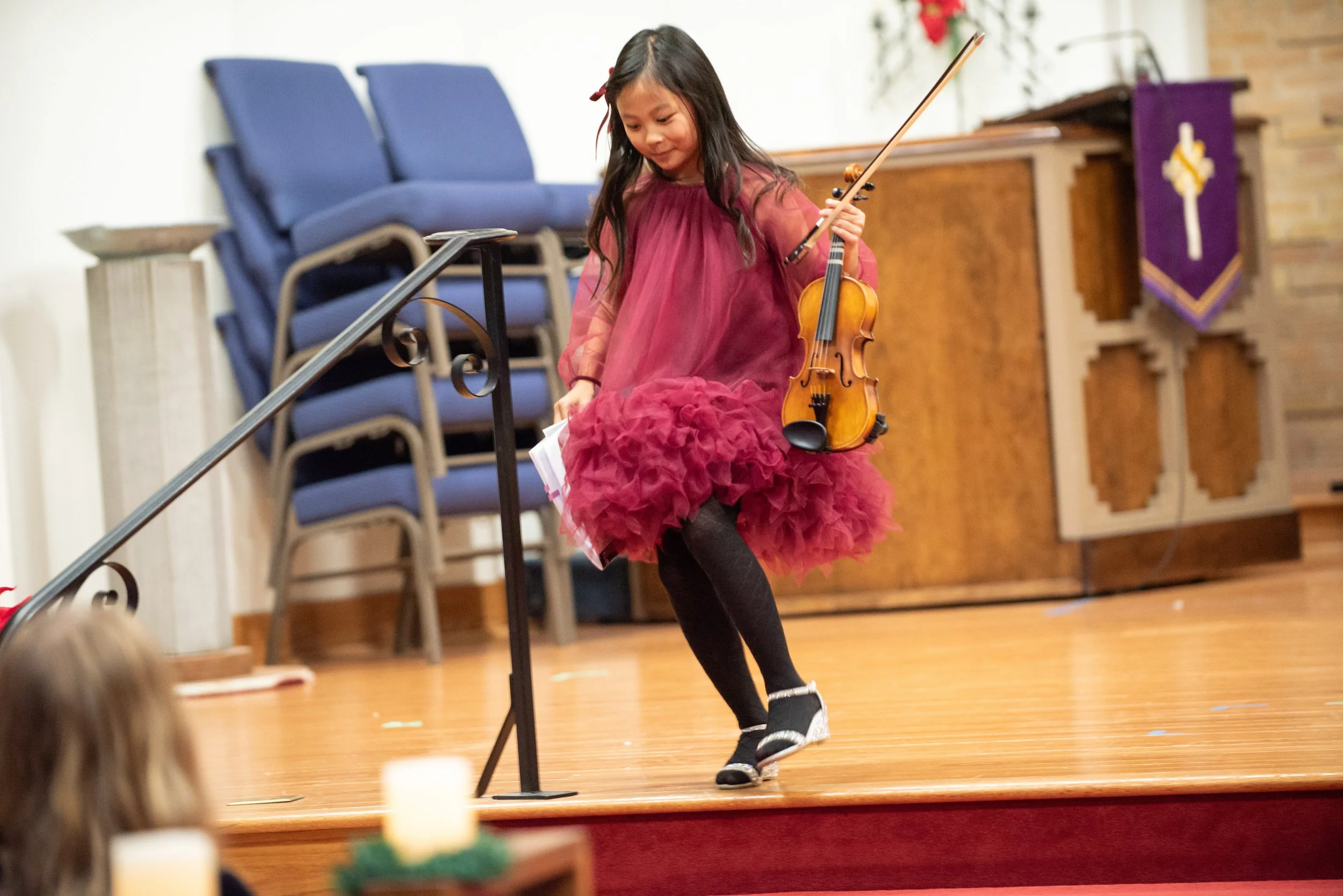 A young girl leaves the stage with excitement after performing in a violin recital