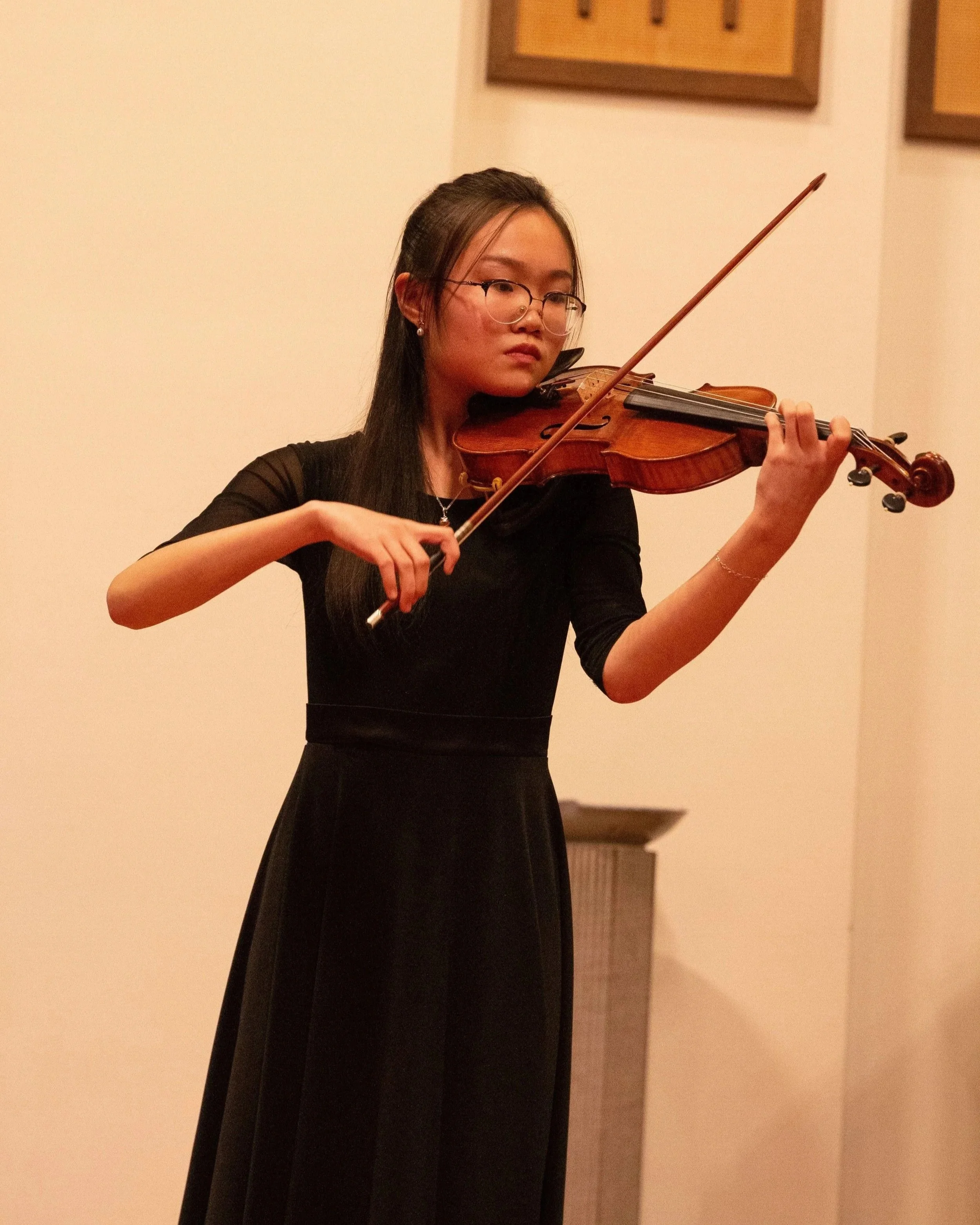 A teenage girl performs violin on stage with focus