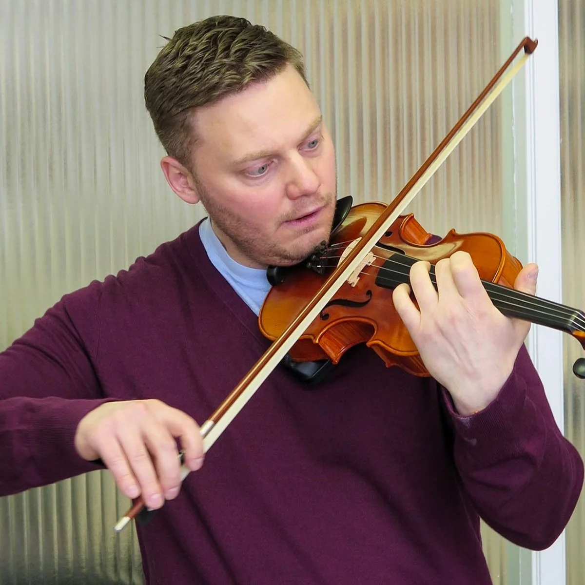 An adult student plays violin in a lesson with peaceful focus