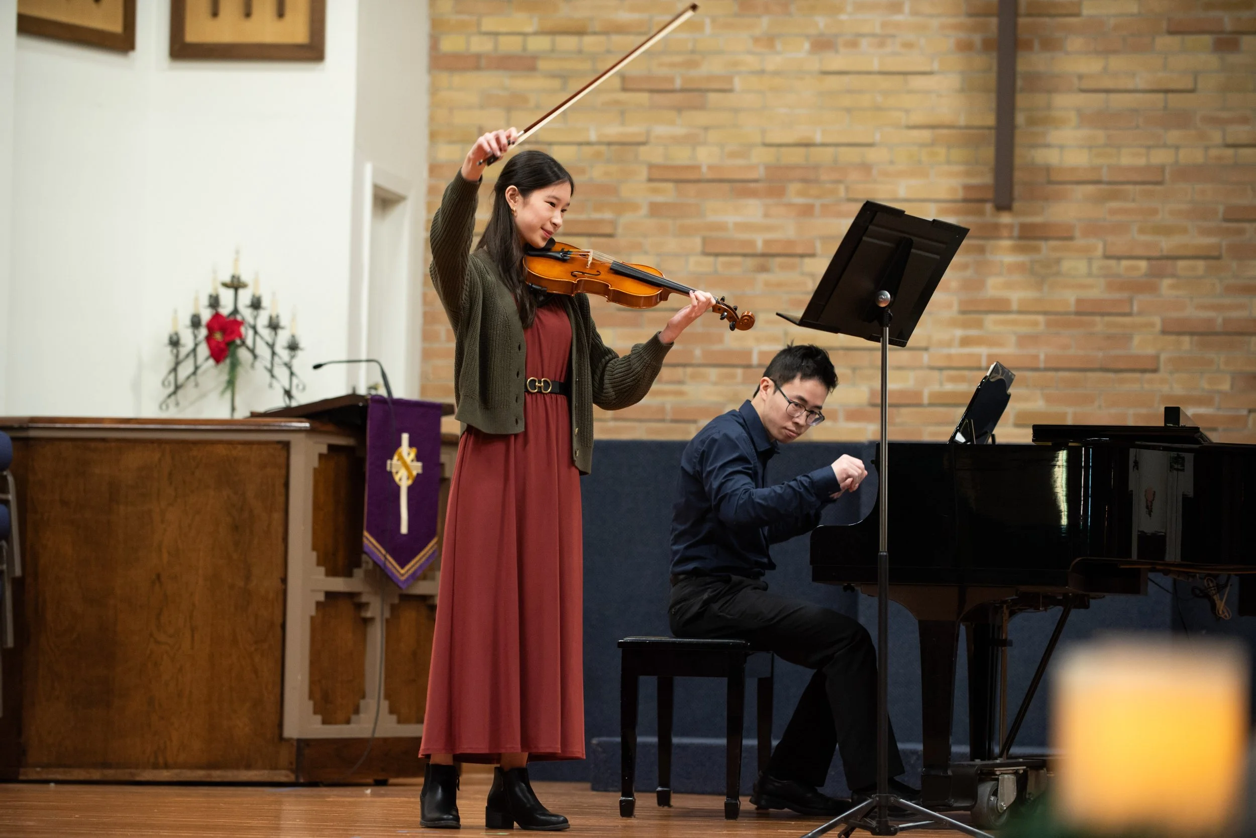 A teenage violinist excitedly finishes performing on stage in a recital with a pianist.