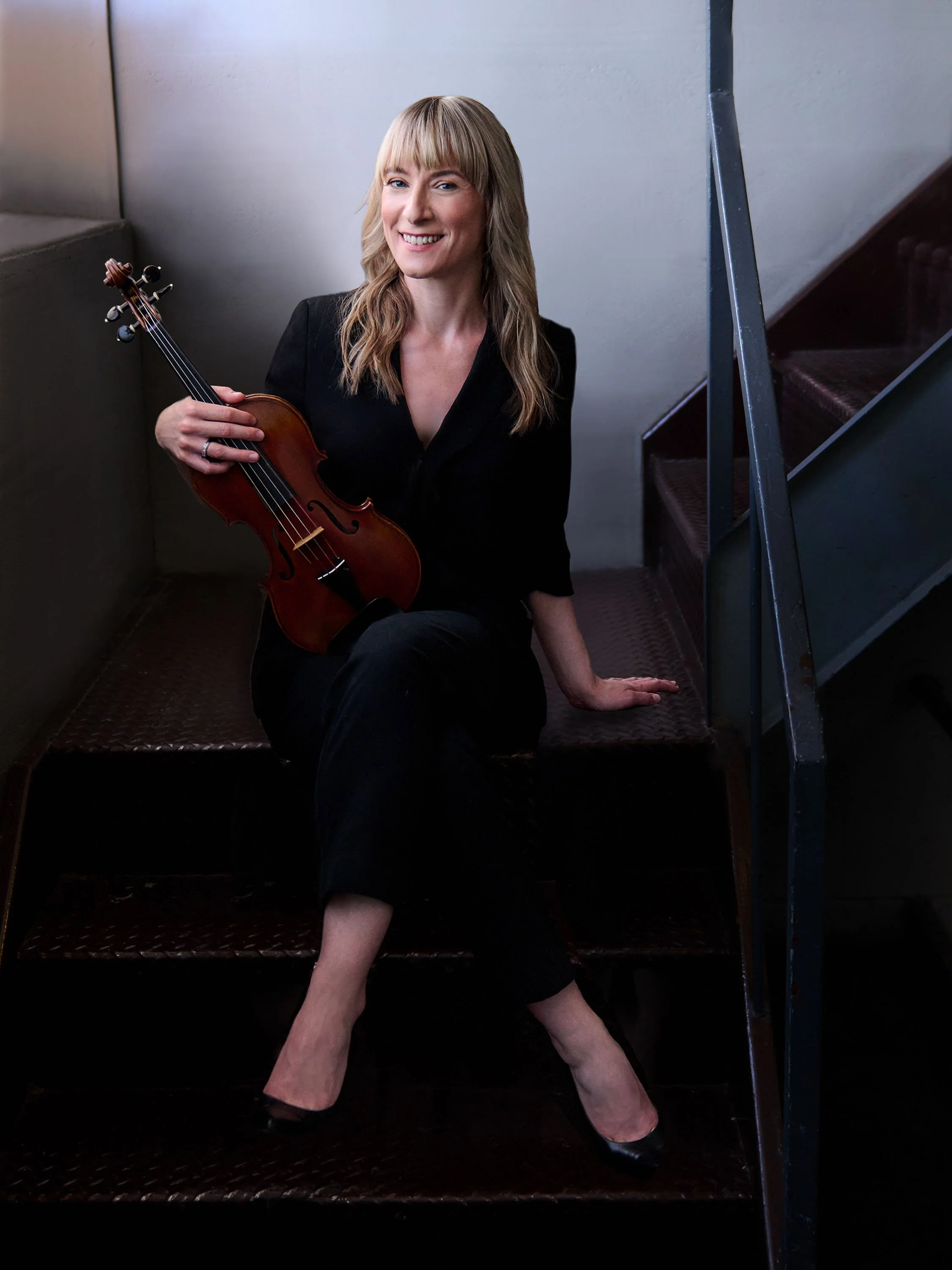 An image of Carmen sitting on the stairs with her violin.