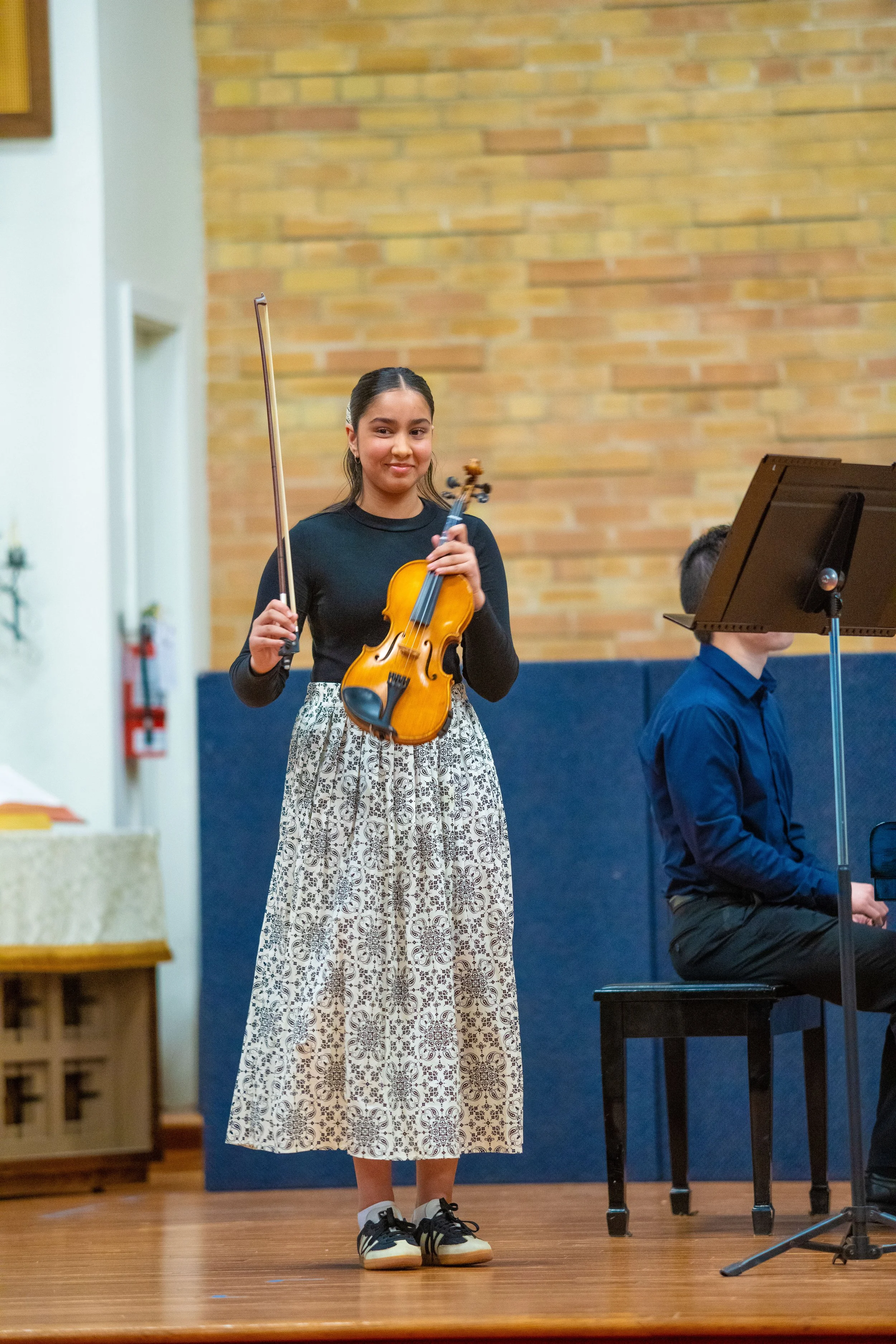 A middle school age girl violinist smiles with happiness after performing on stage at a recital.