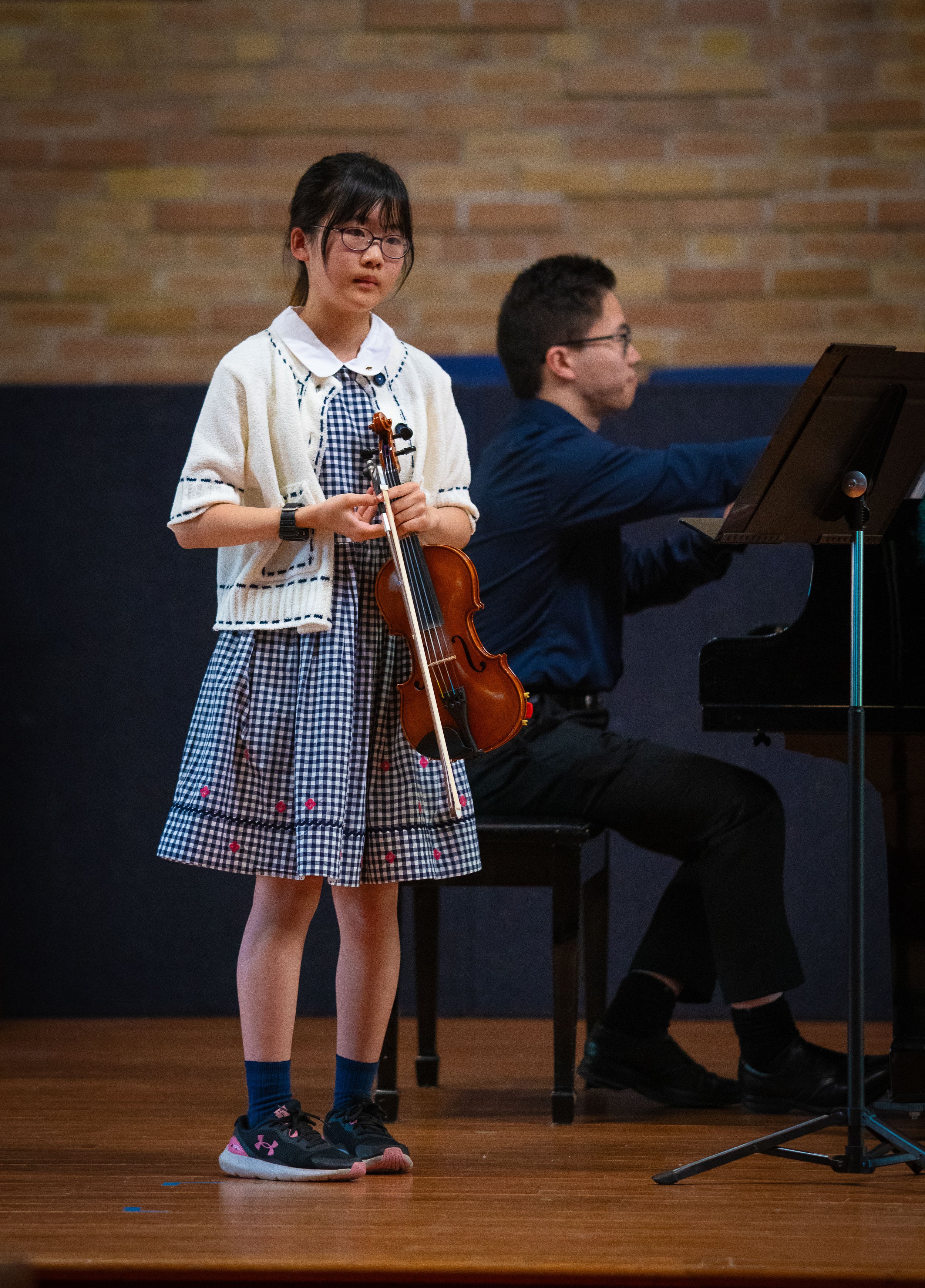 A young girl looks reflectively at the audience after performing at a violin concert