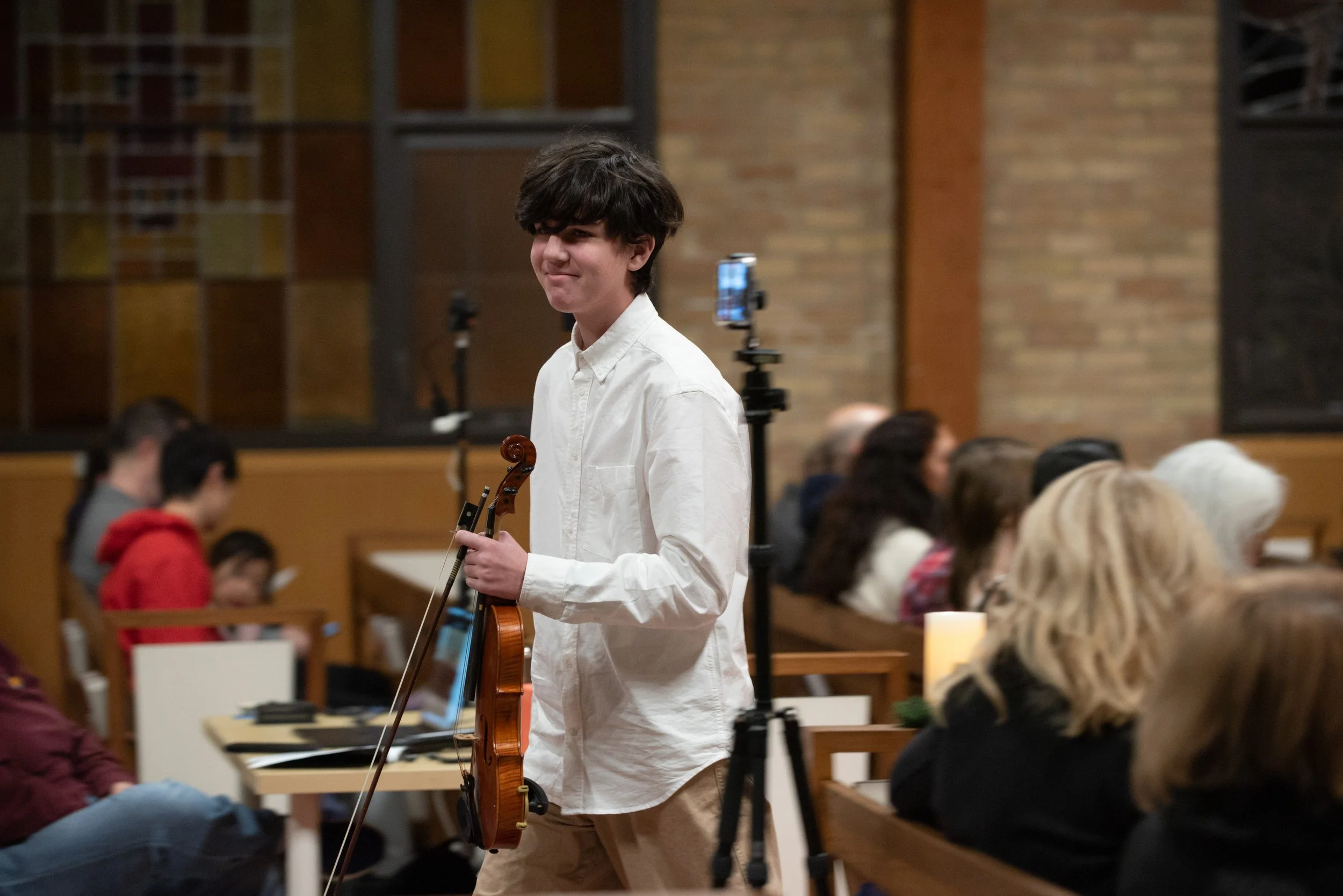 A middle school age violin player proudly walks off stage with a smile after performing in a recital.