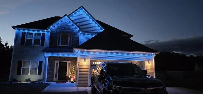 House decorated with blue Christmas lights at night, with a black pickup truck parked in front.