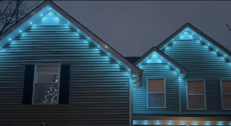 The image shows the exterior of a house decorated with blue string lights along the roofline at night.
