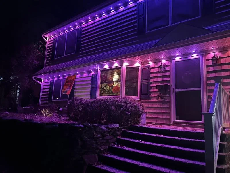A house decorated with purple and pink neon lights at night, with stairs leading to the front door.