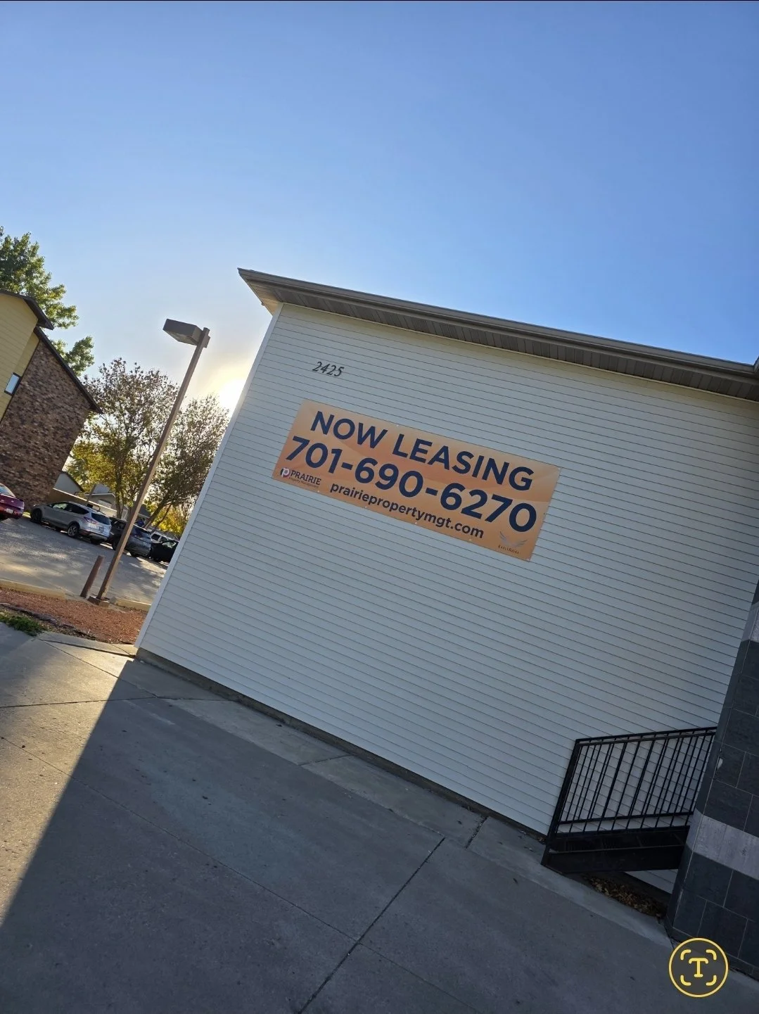 A building with a sign that reads 'Now Leasing' and a phone number 701-690-6270, located at 2425, with parking lot and trees in the background.