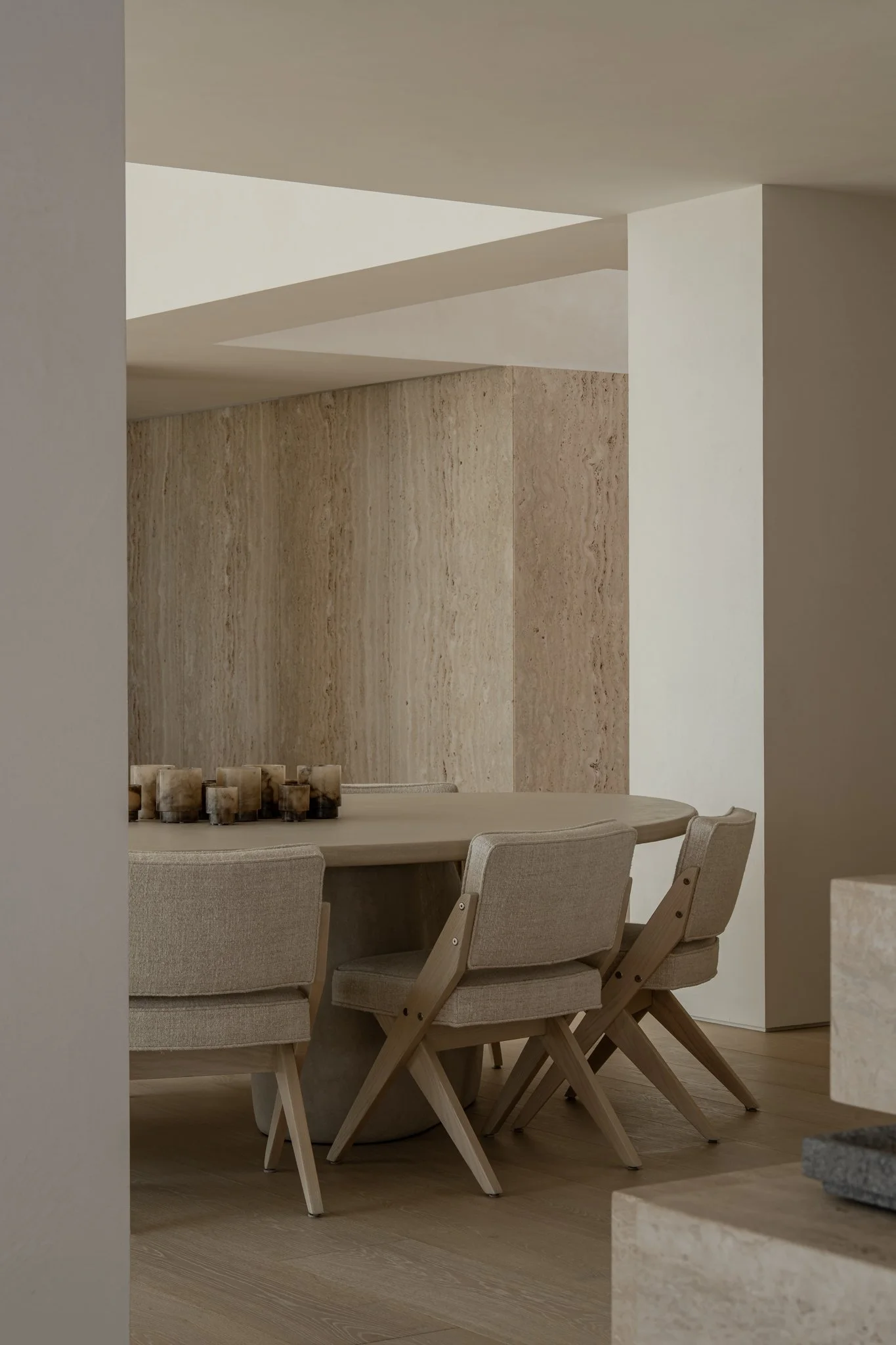 Minimalist dining room with a round table, beige upholstered chairs, and a textured beige wall.