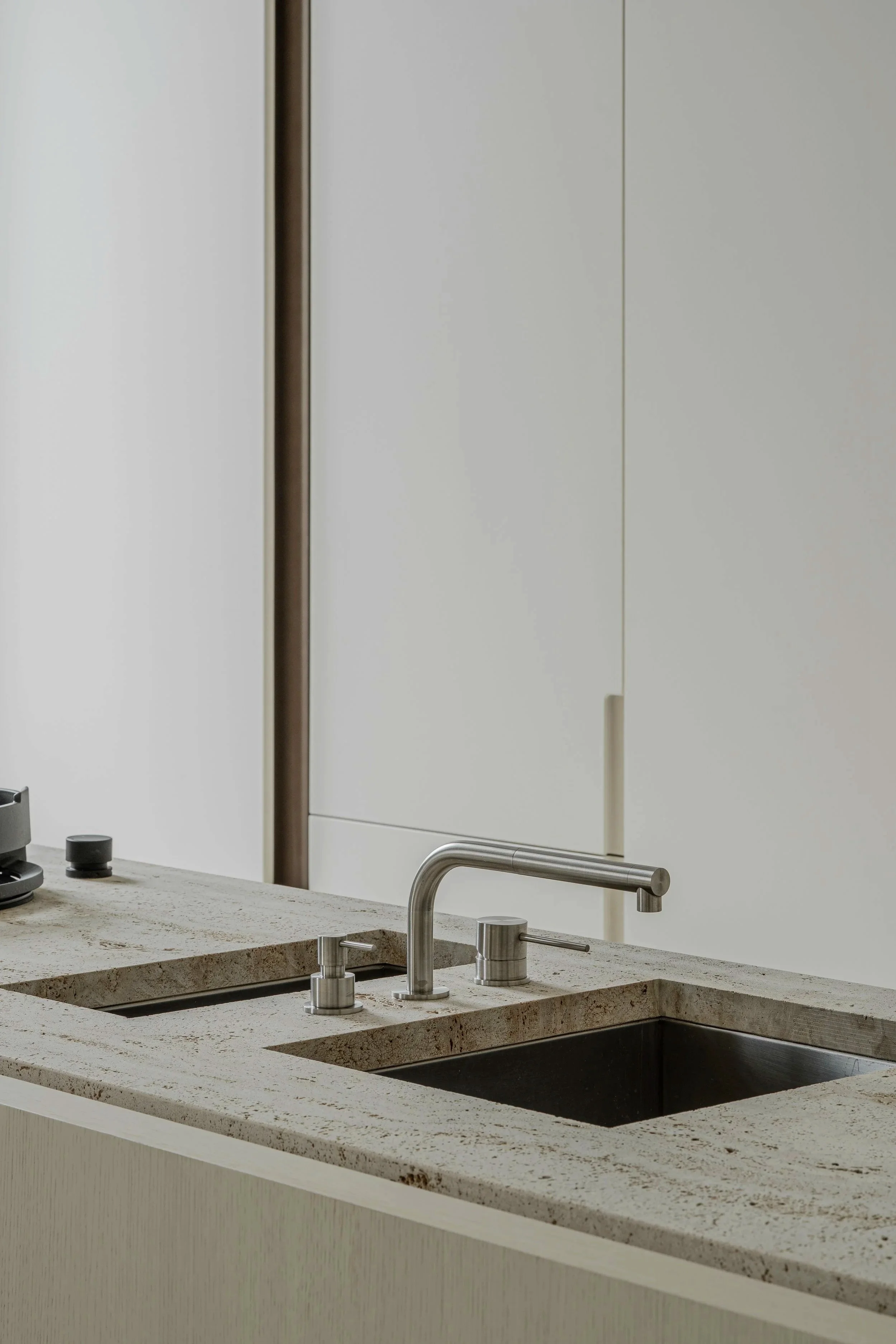 Close-up of a modern kitchen sink with a metal faucet and beige granite countertop, with a white cabinet in the background.