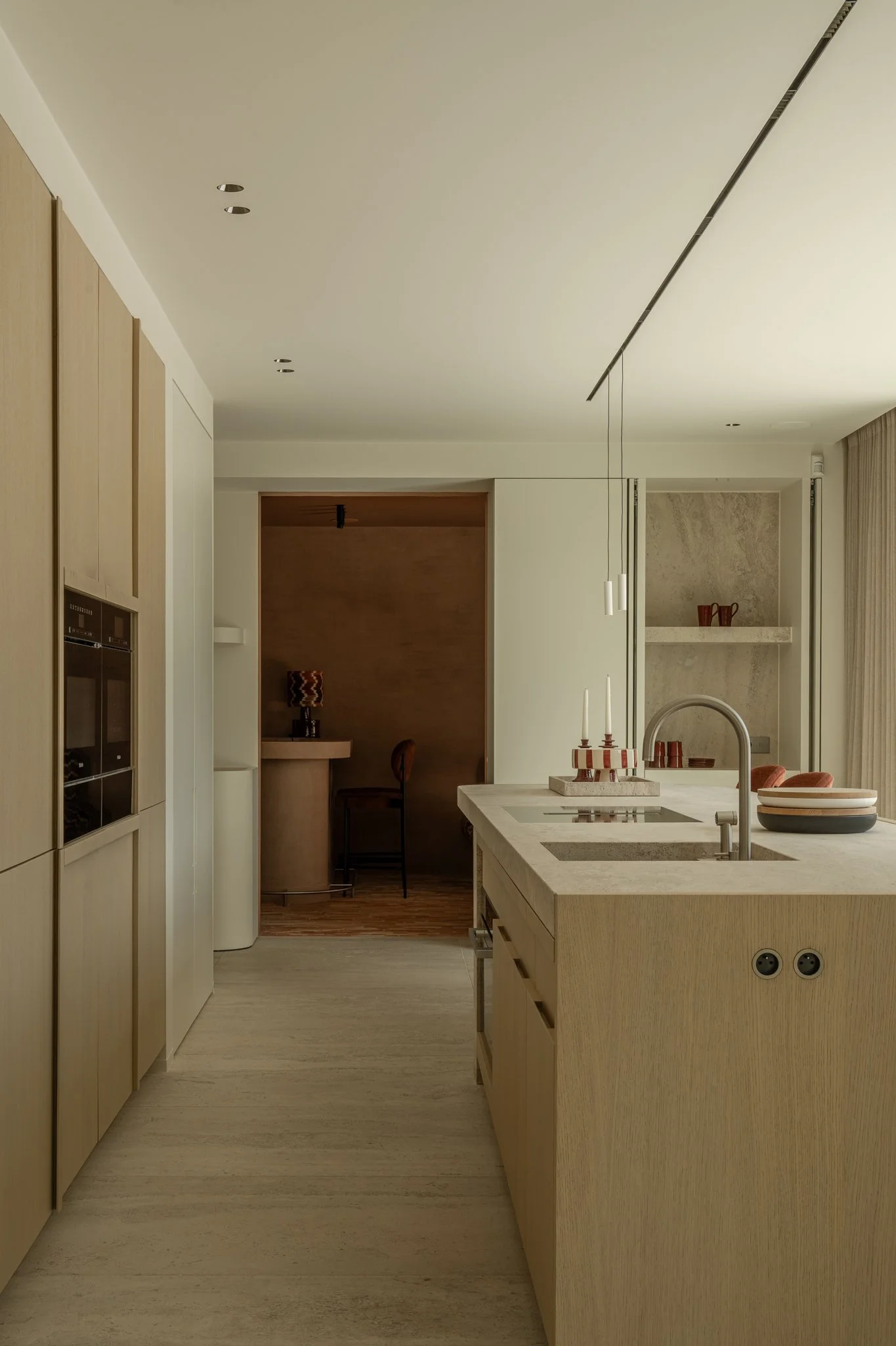 Modern kitchen with light wood cabinetry, a central island with a sink, and minimal decor in neutral tones.