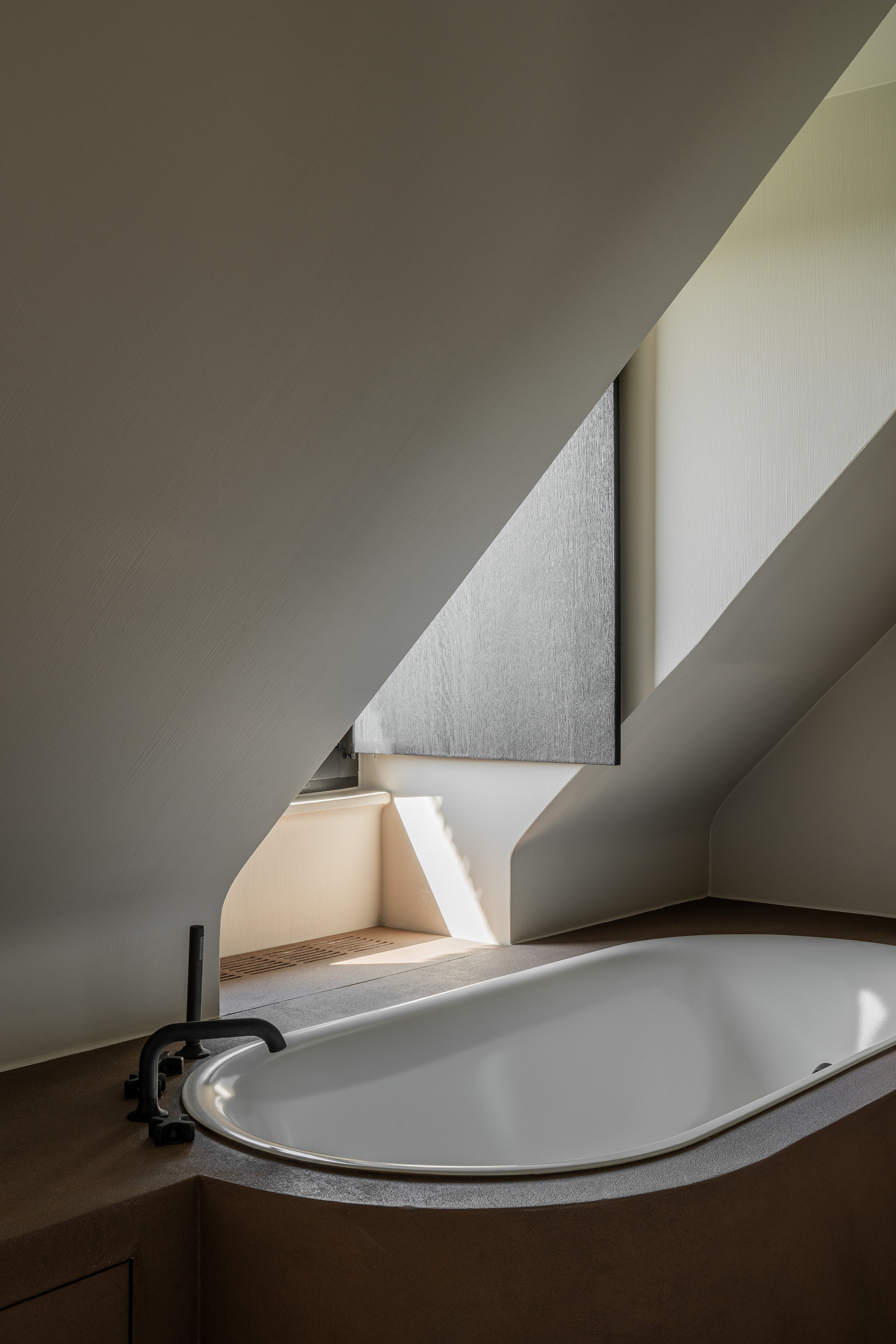Small bathtub under a sloped ceiling with a window and natural light.