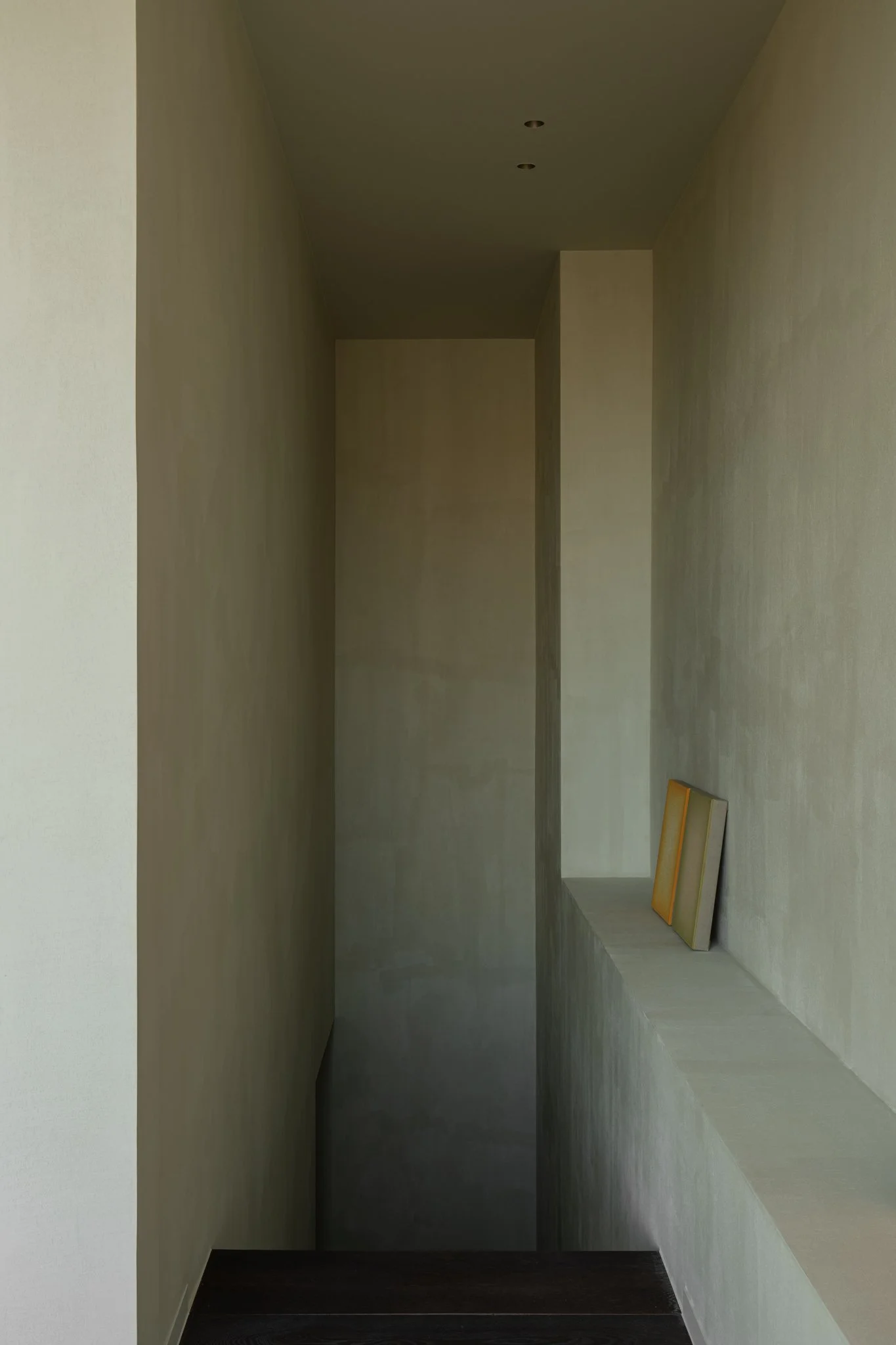 Minimalist interior with beige textured walls, dark flooring, and two framed pictures resting on a ledge.