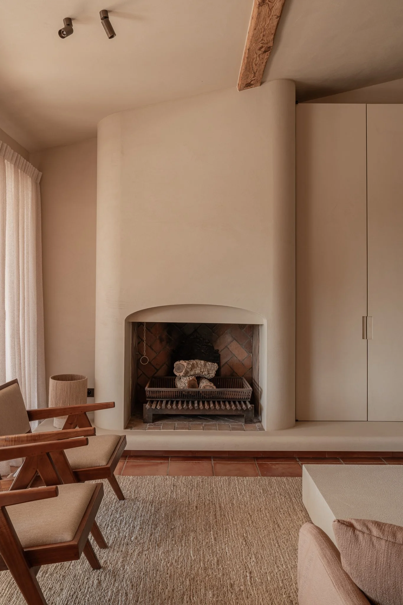Interior of a living room with a curved white fireplace, wooden furniture, beige carpet, and neutral-toned decor.