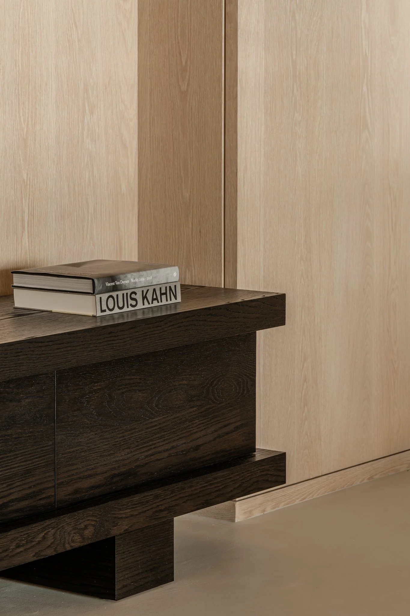 Two books stacked on a dark wooden cabinet with a light wood wall in the background.